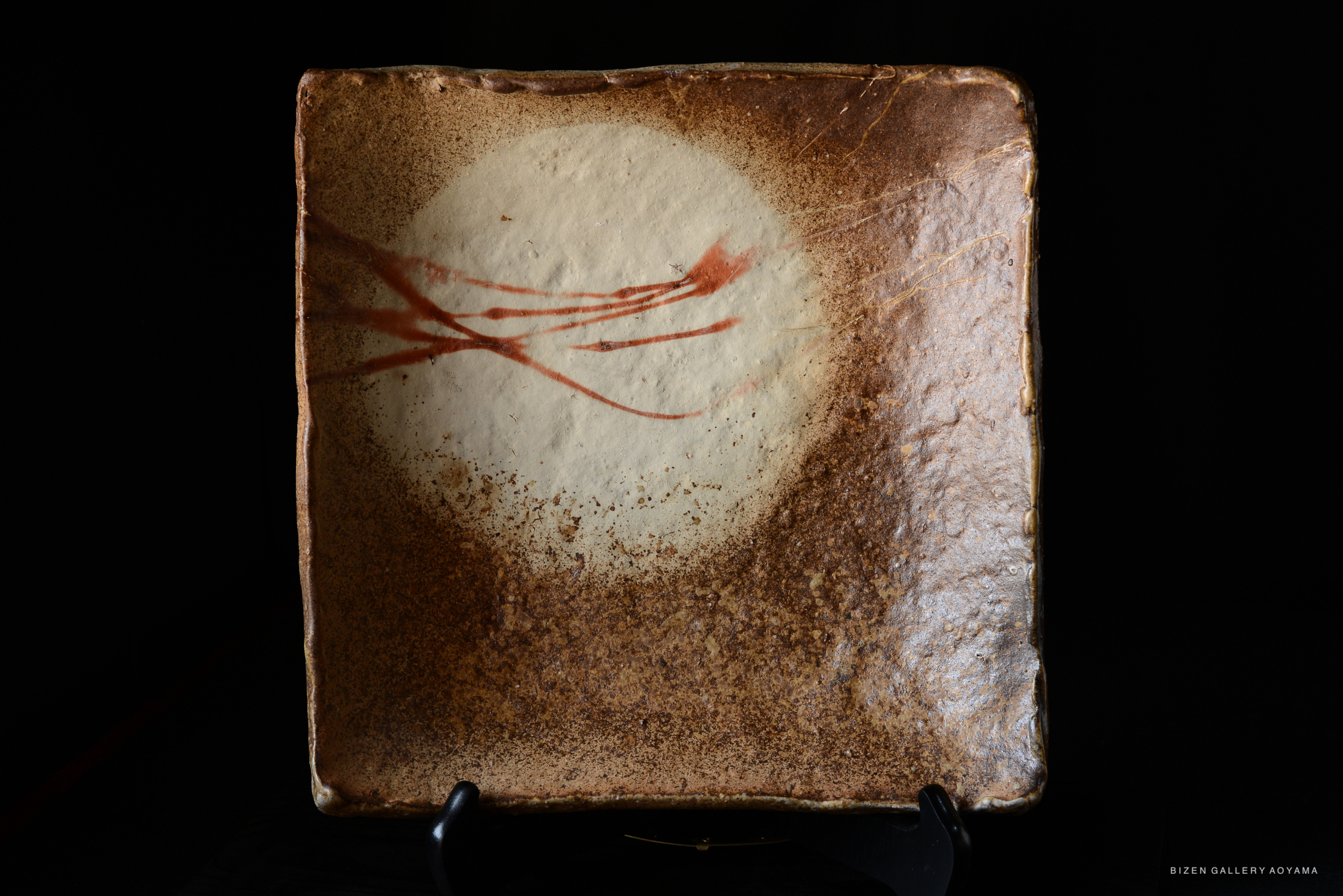 Bizen kakuzara, a square-shaped ceramic plate with a textured brown surface and a white circular design, featuring red brush strokes.