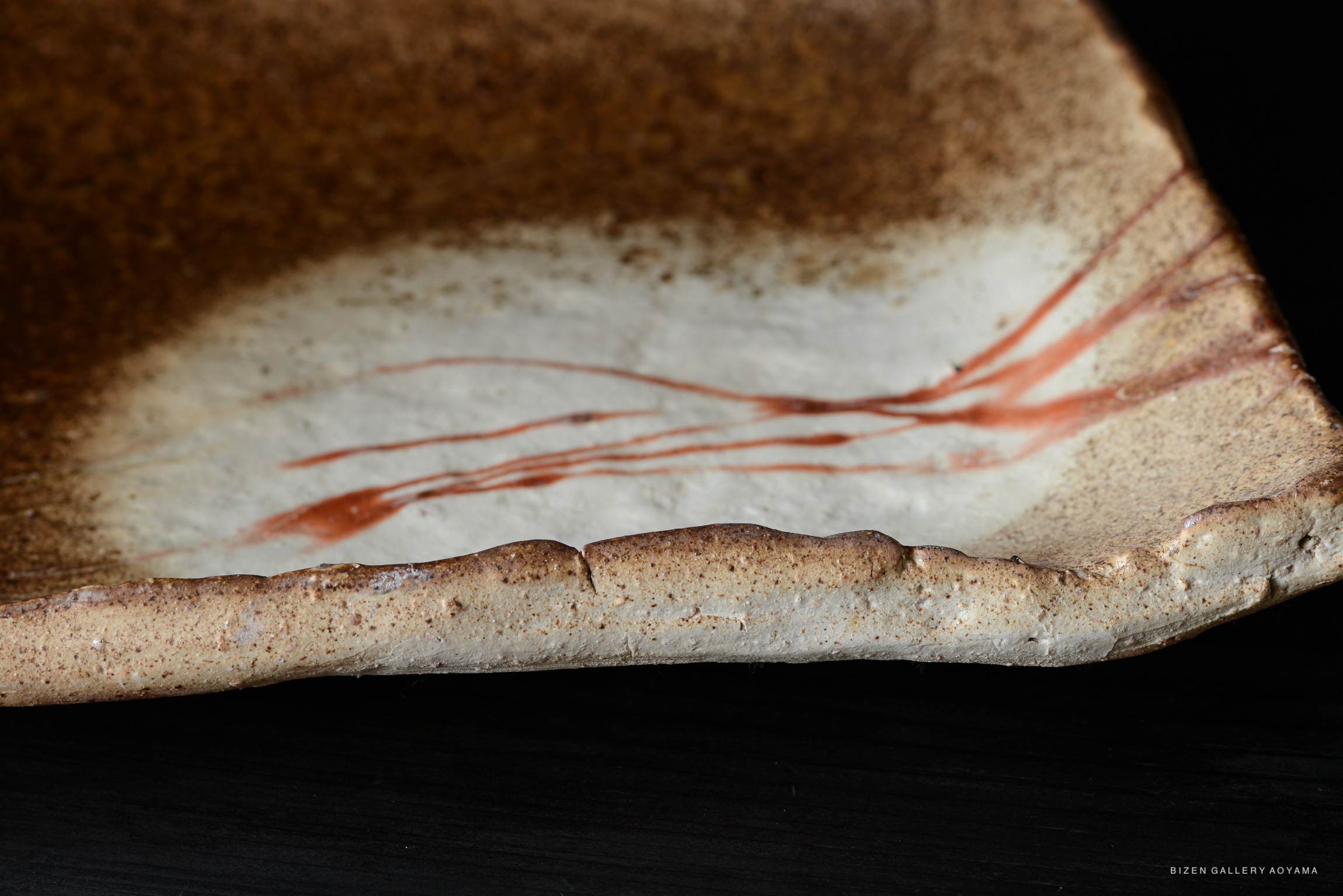 Close-up of a Bizen pottery plate with a textured surface and subtle red markings.