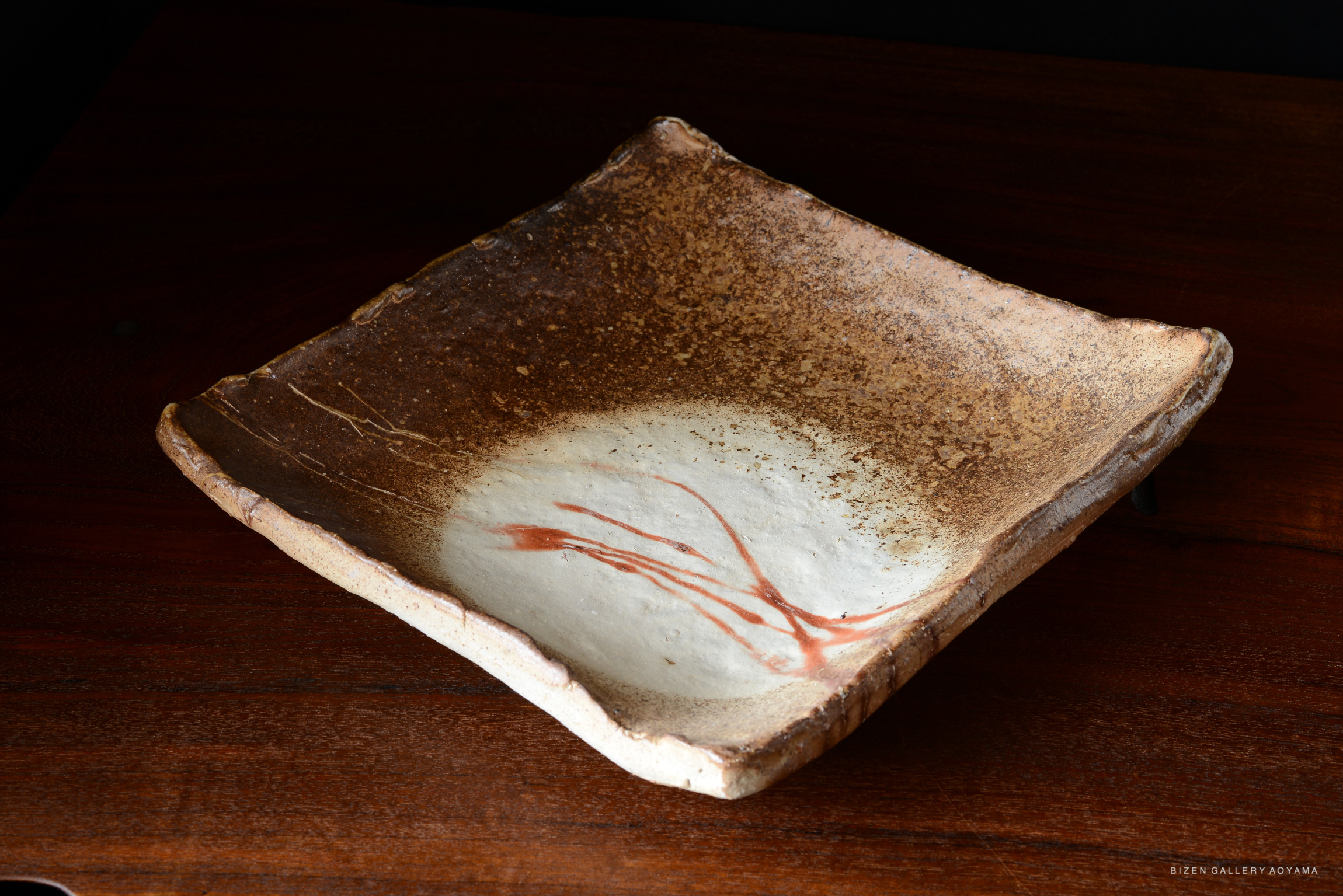 A handcrafted Bizen pottery plate featuring a textured brown exterior and a smooth white interior with a red streak design.