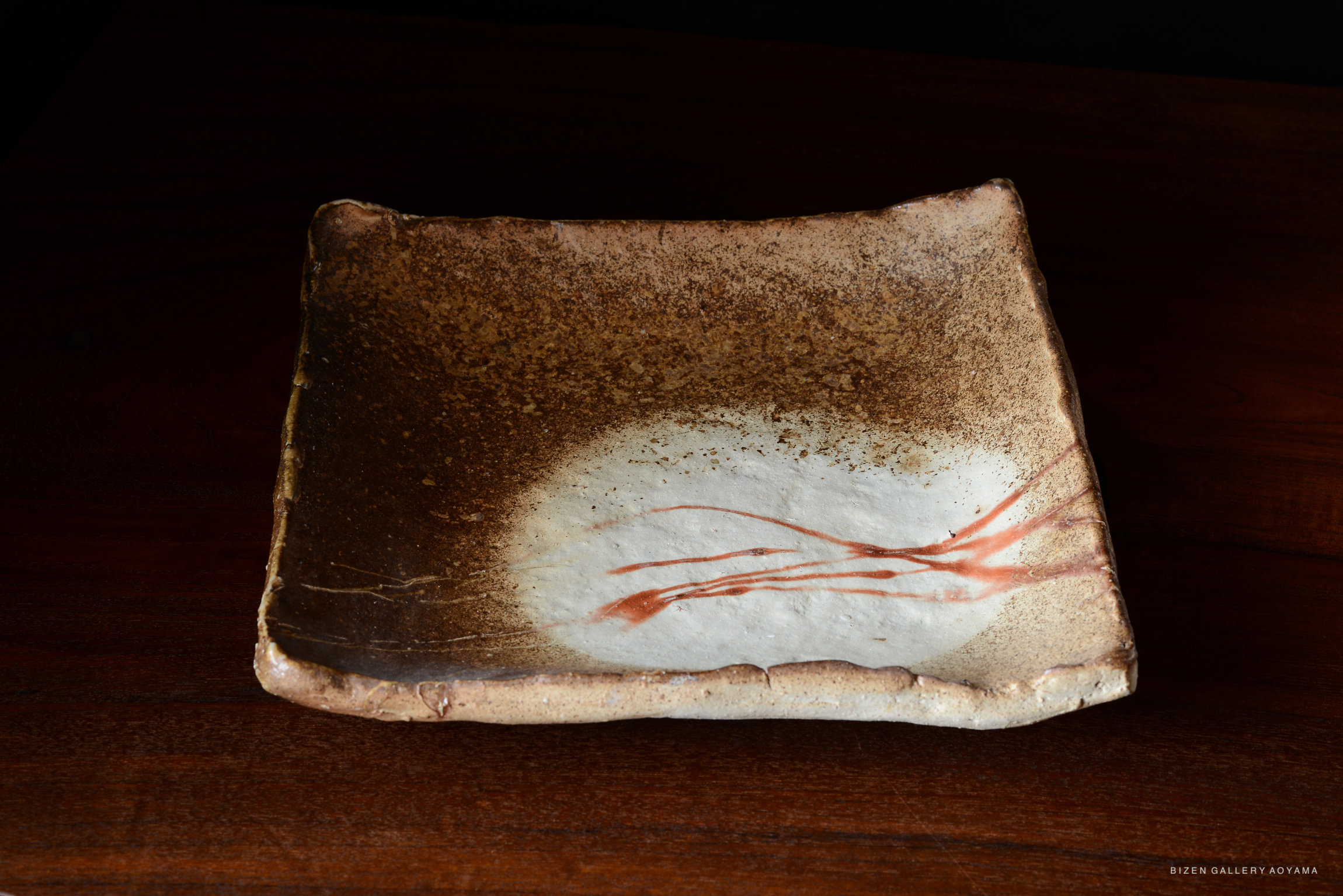 A square, rustic Bizen pottery plate with a textured brown exterior and a white center featuring delicate red brush strokes.