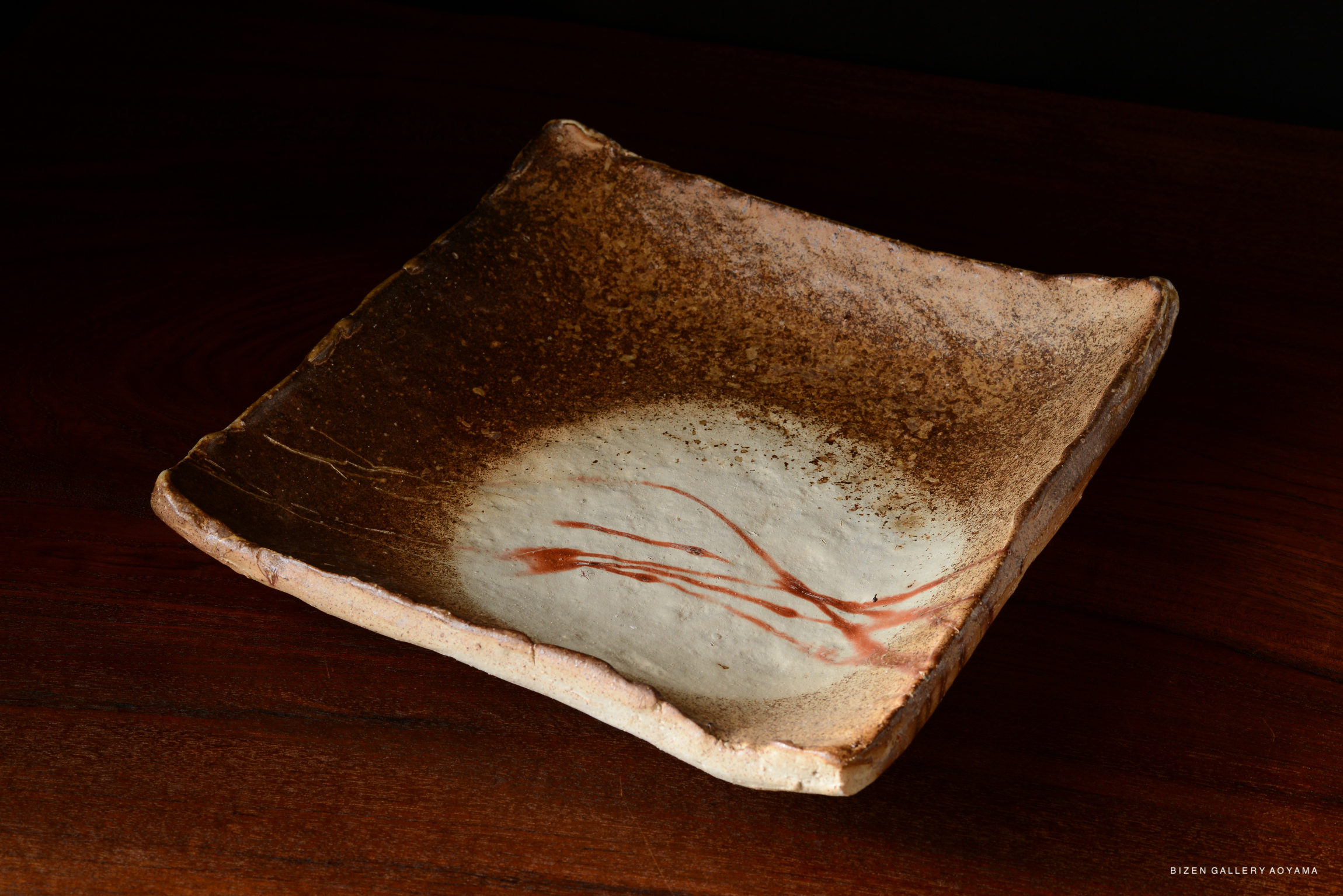 A unique Bizen pottery plate with a textured, earthy surface and a cream-colored center featuring subtle red streaks.