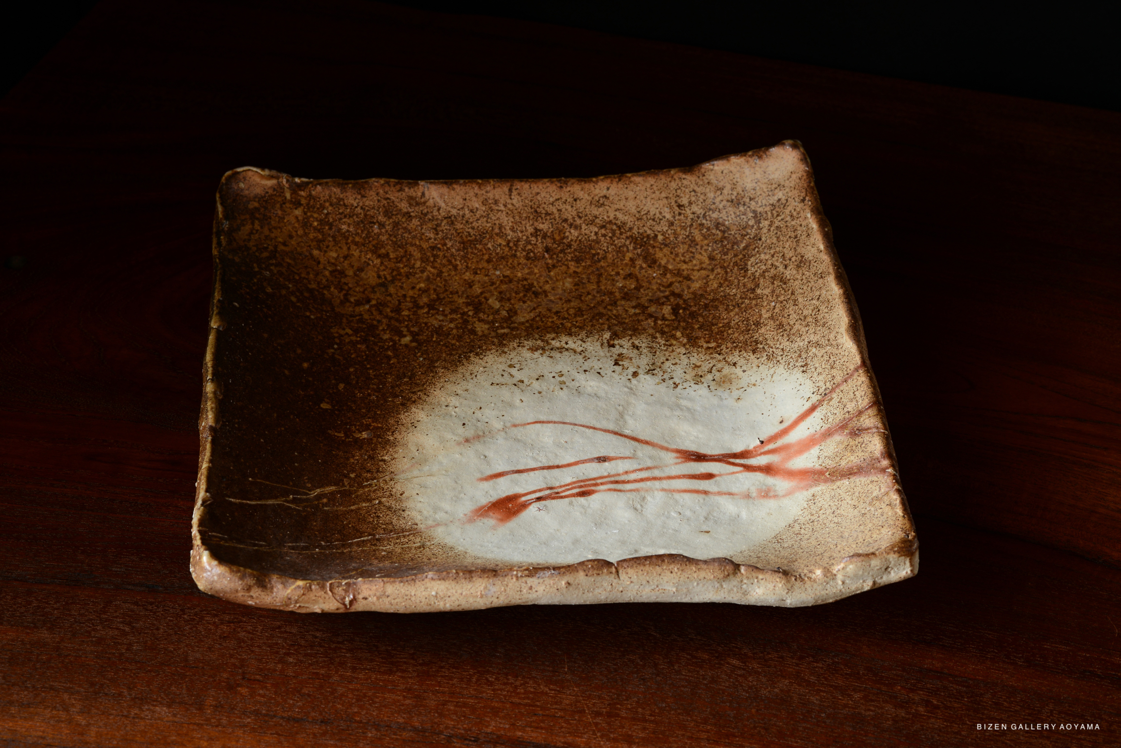 A handcrafted Bizen pottery plate featuring a textured brown surface with a white center and delicate red lines.