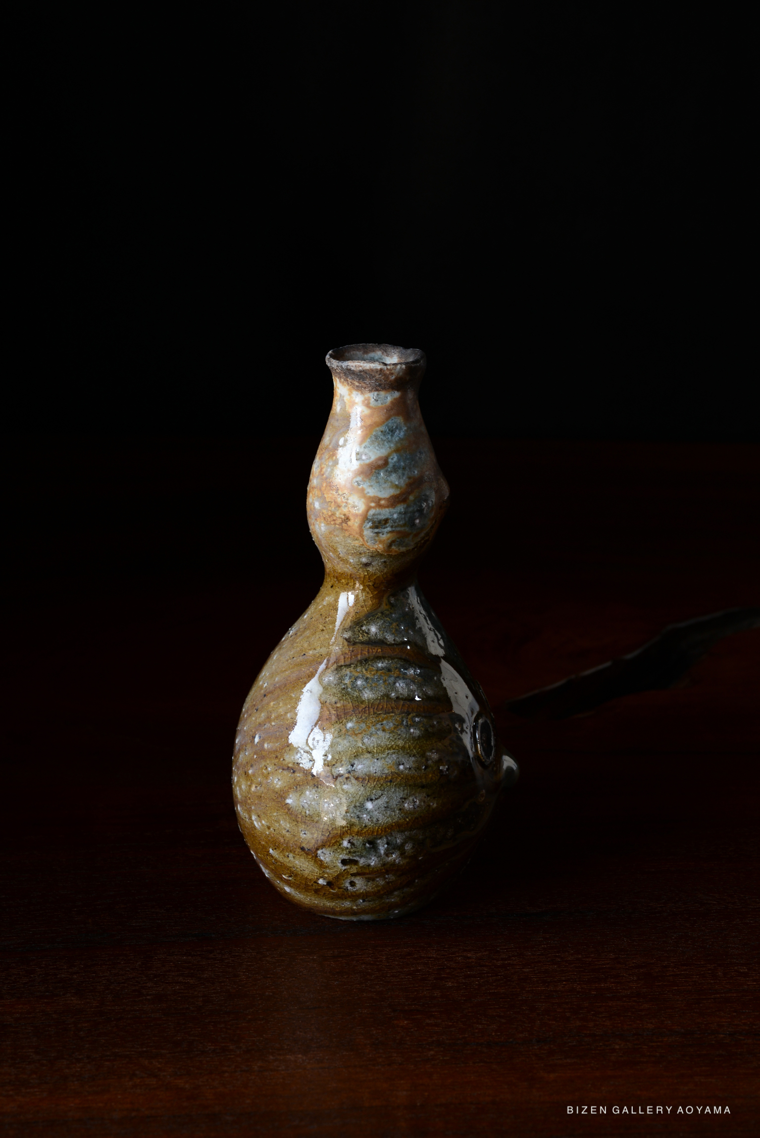 A unique pottery vessel with a rounded body and narrow neck, displaying a combination of earthy tones, including browns and blues, set against a dark background.