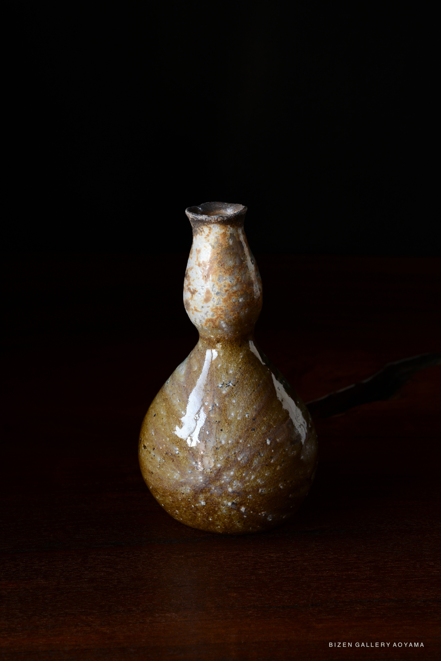 A small, decorative Bizen pottery bottle with a rounded base and narrow neck, featuring a natural earthy glaze, set against a dark background.