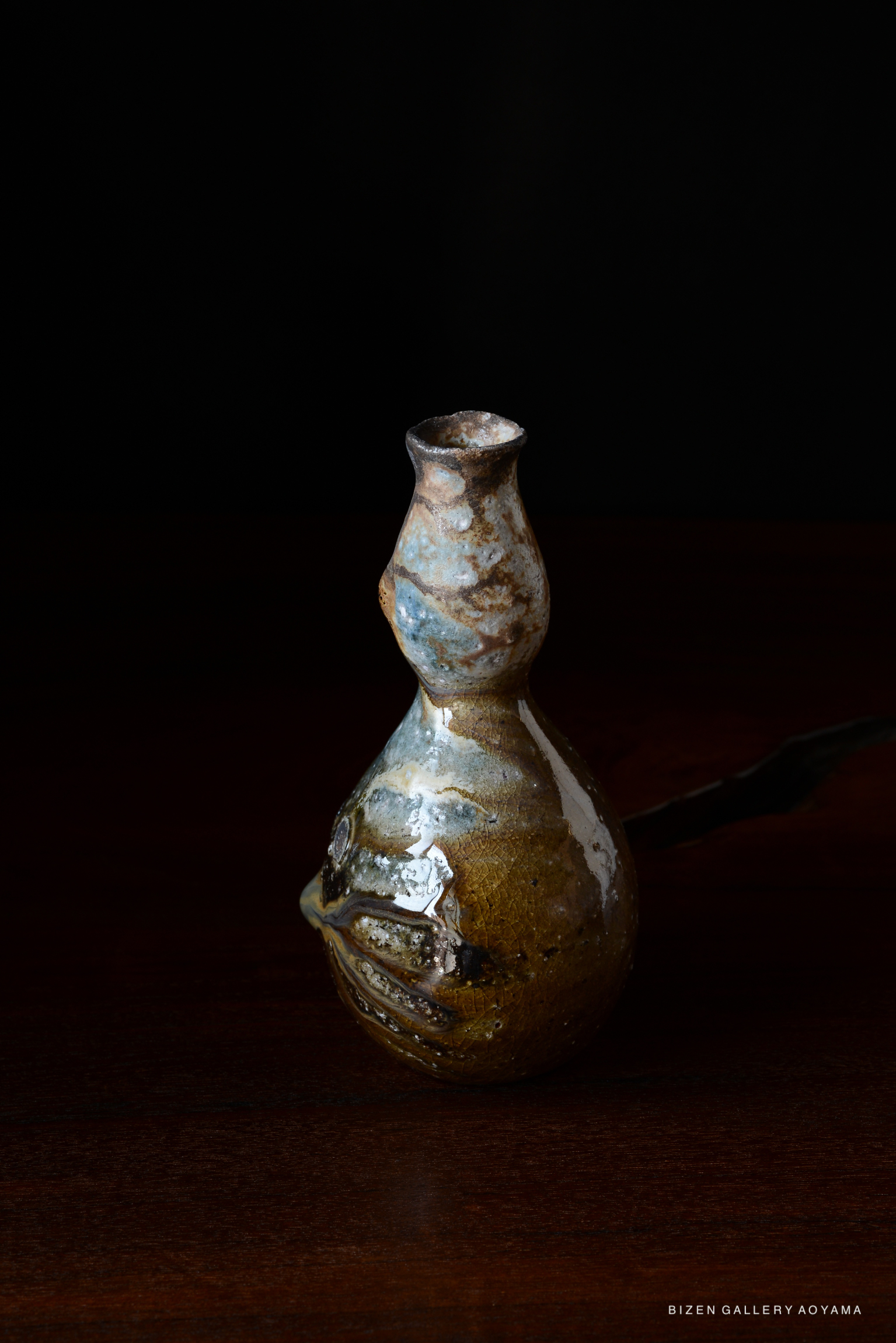 A decorative ceramic bottle with a unique shape, featuring a glossy surface and earthy colors, placed against a dark background.