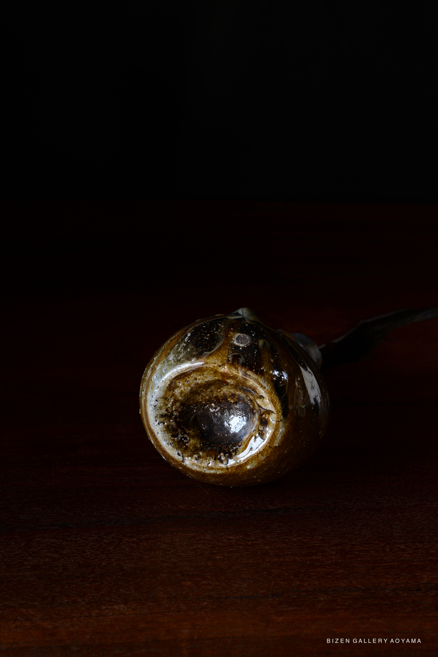 A close-up image of a ceramic vessel with a glossy, textured surface, set against a dark background.