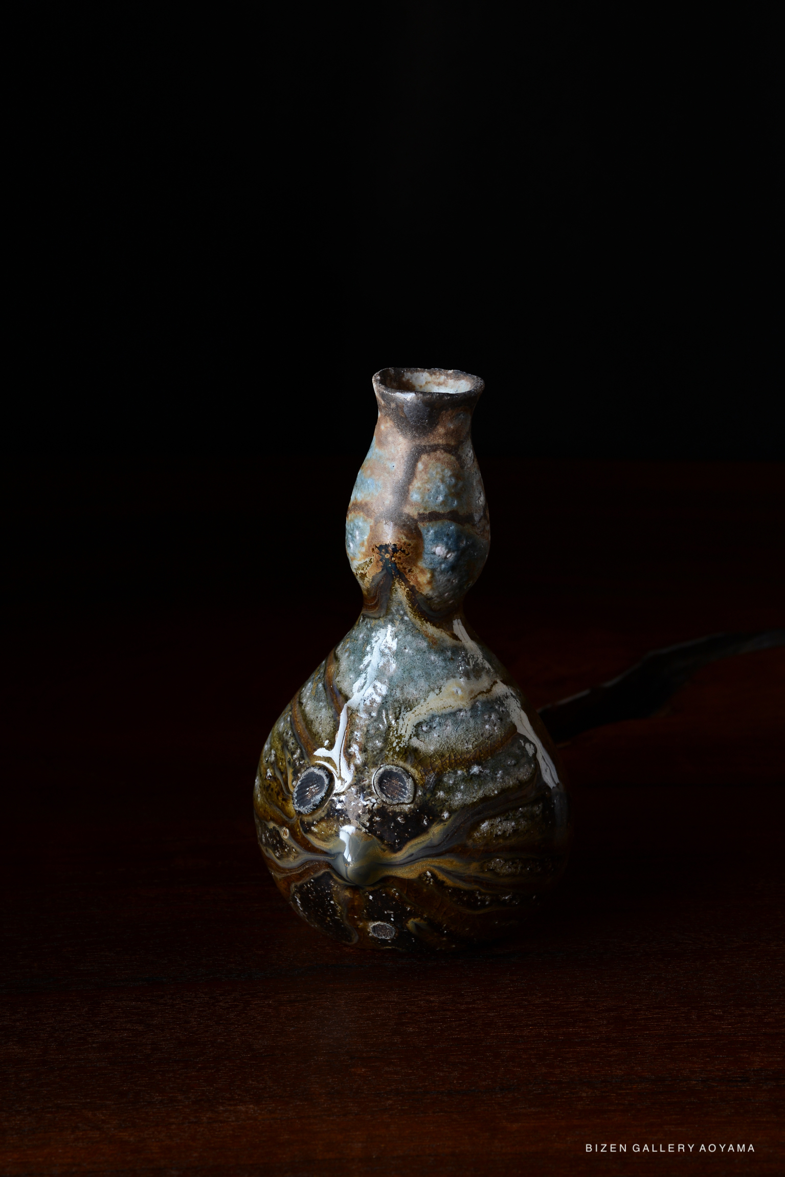 A decorative ceramic bottle with a unique shape and colorful glaze, set against a dark background.