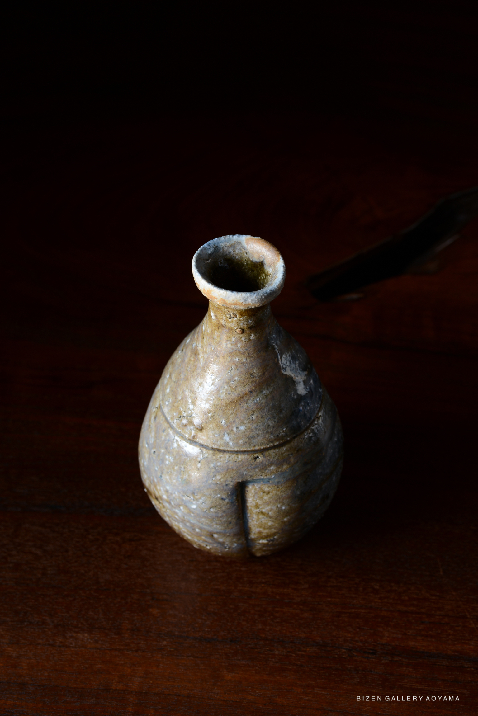 A unique, handmade Bizen pottery vase with a rounded base and narrow neck, resting on a wooden surface.