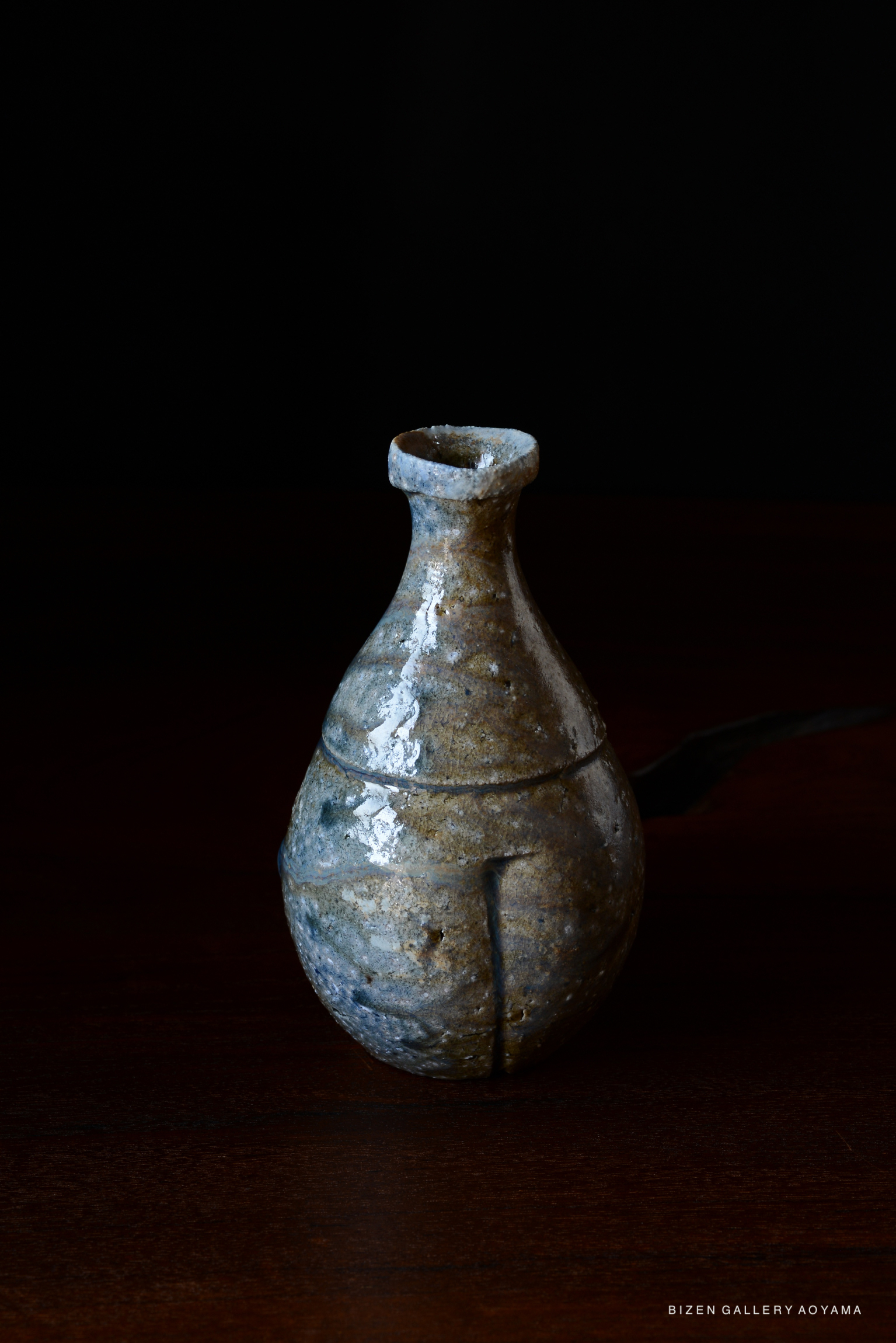 A handcrafted Bizen pottery vase with a rounded body and a narrow neck, displayed against a dark background.
