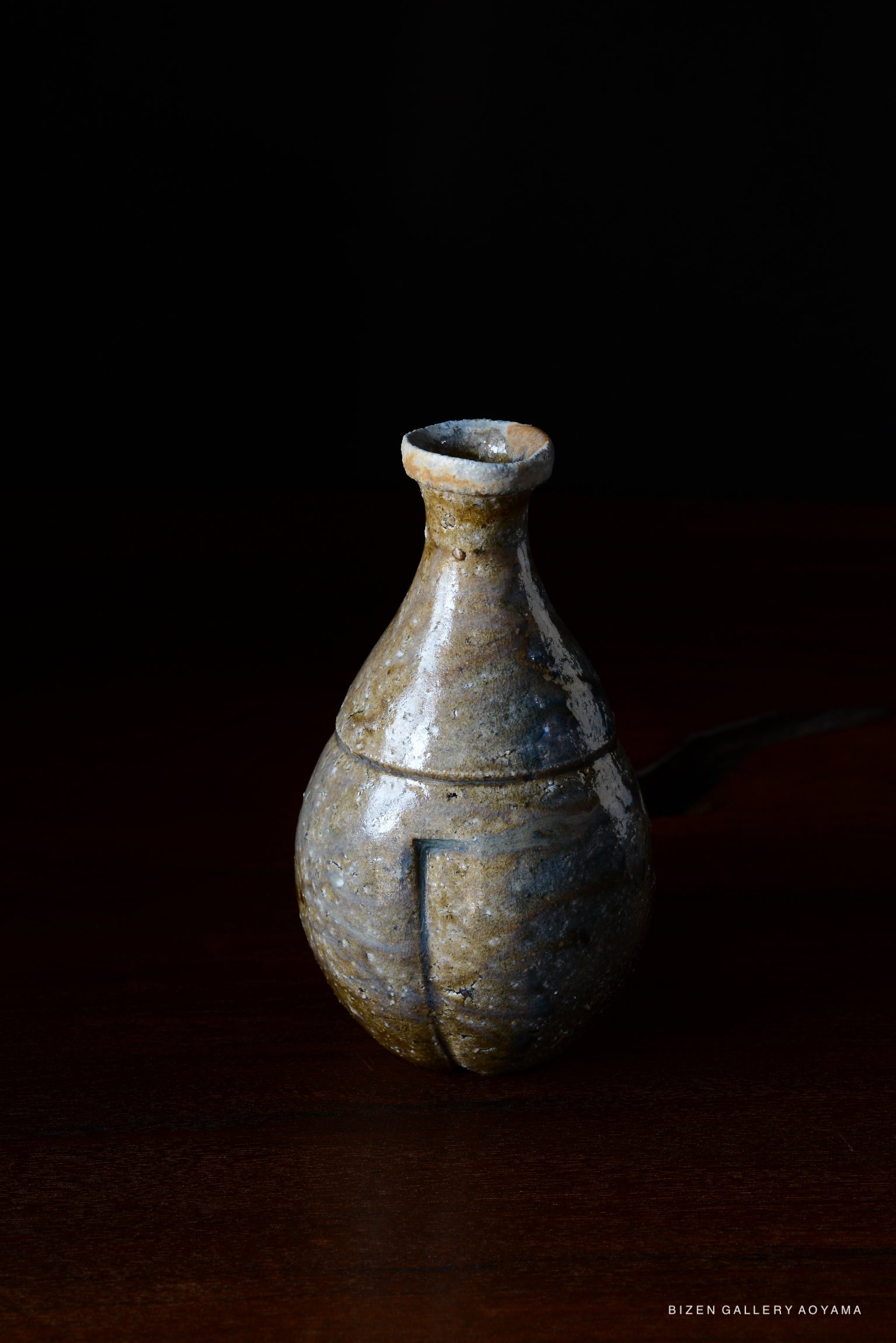 A traditional Bizen pottery vase with a rounded body and narrow neck, displayed on a wooden surface against a dark background.