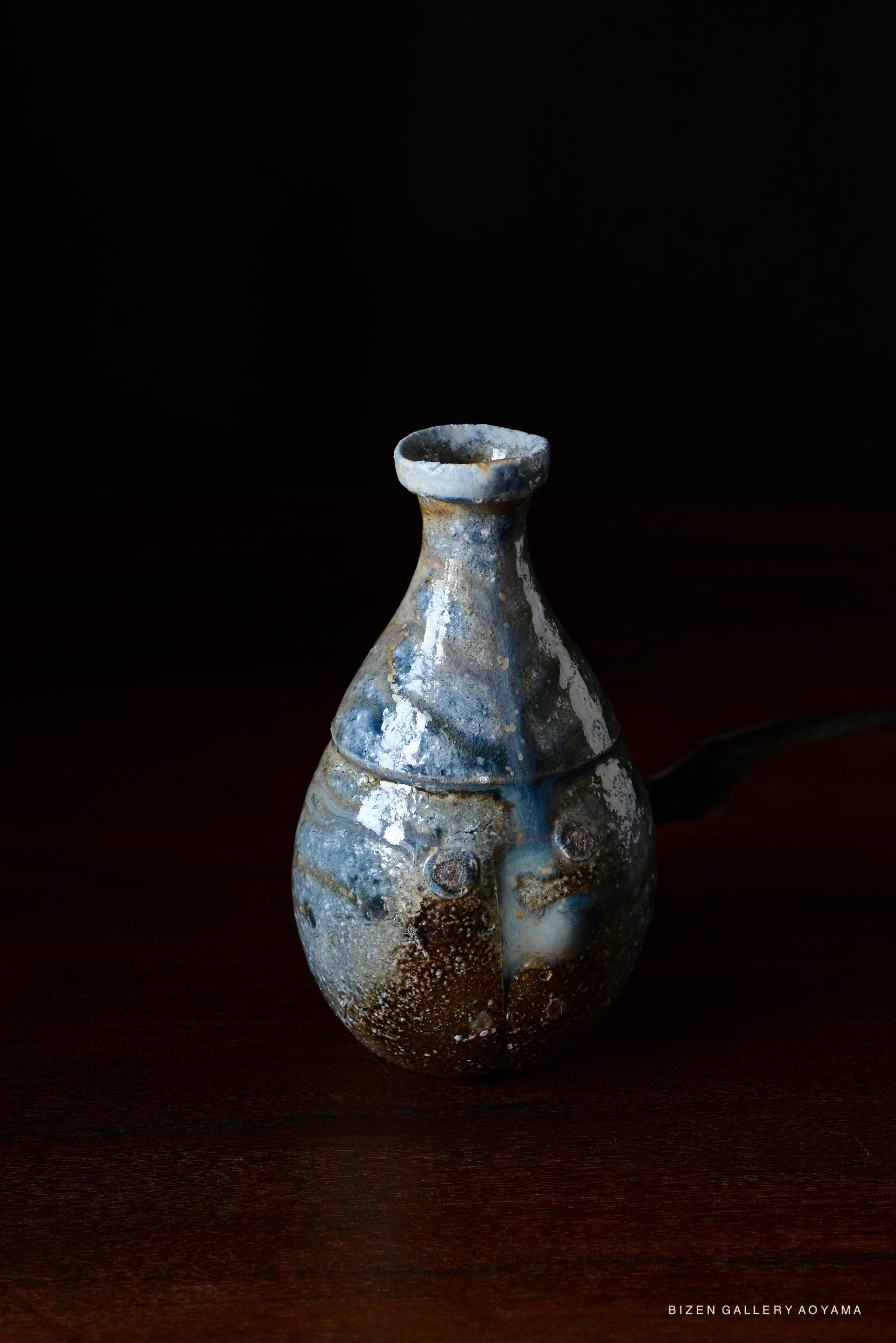 A handcrafted Bizen pottery vessel with a unique texture and a blend of blue and earthy tones, displayed against a dark background.