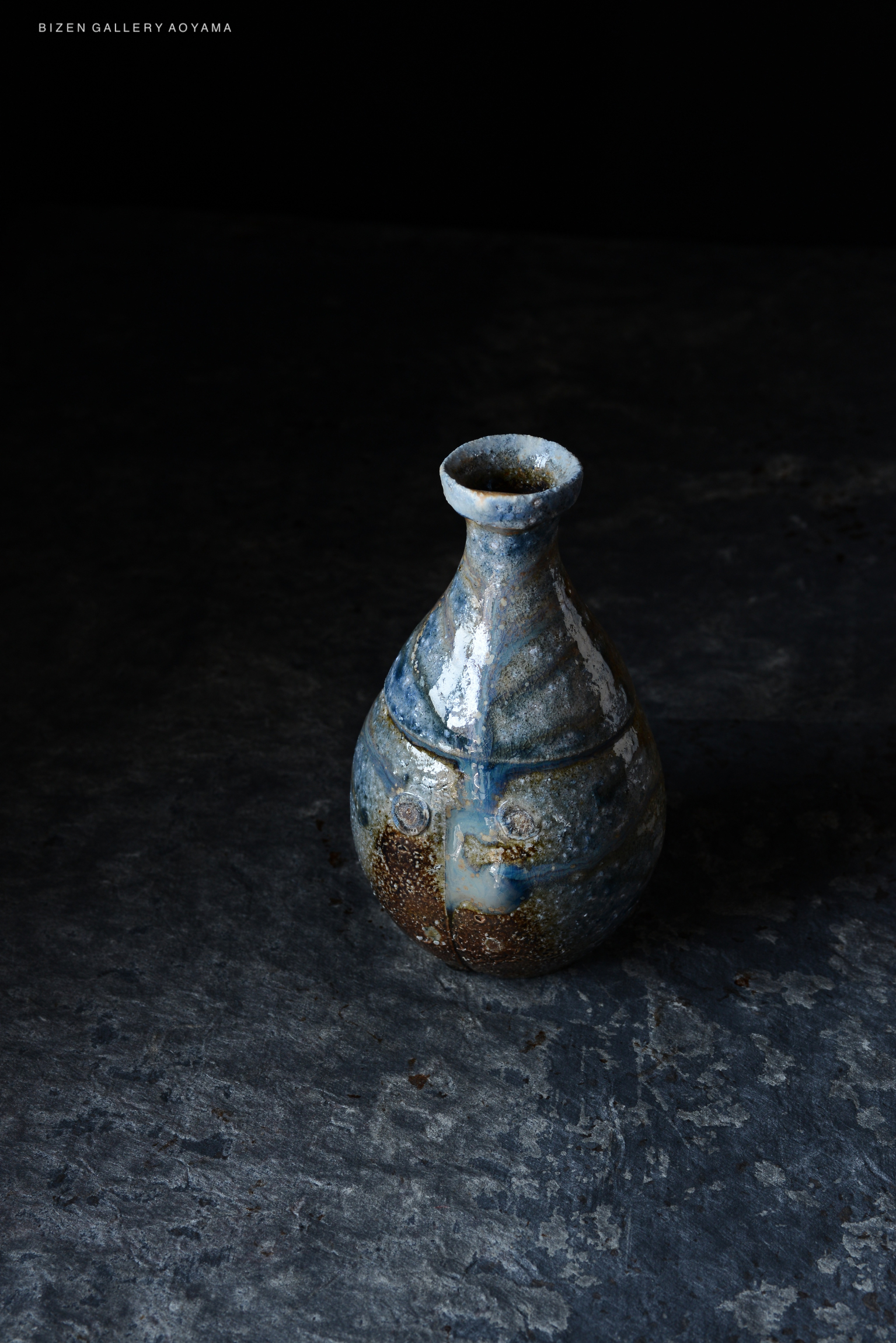 A ceramic vase with a unique blue and brown glaze, set against a dark background.