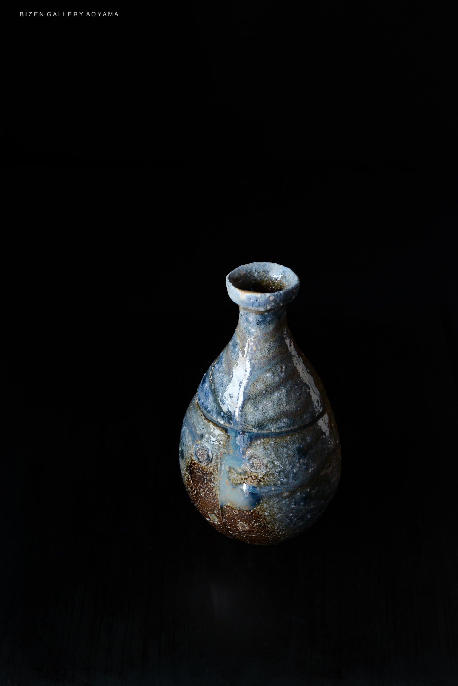 A handcrafted Bizen pottery vase with a unique blue and brown glaze, set against a black background.