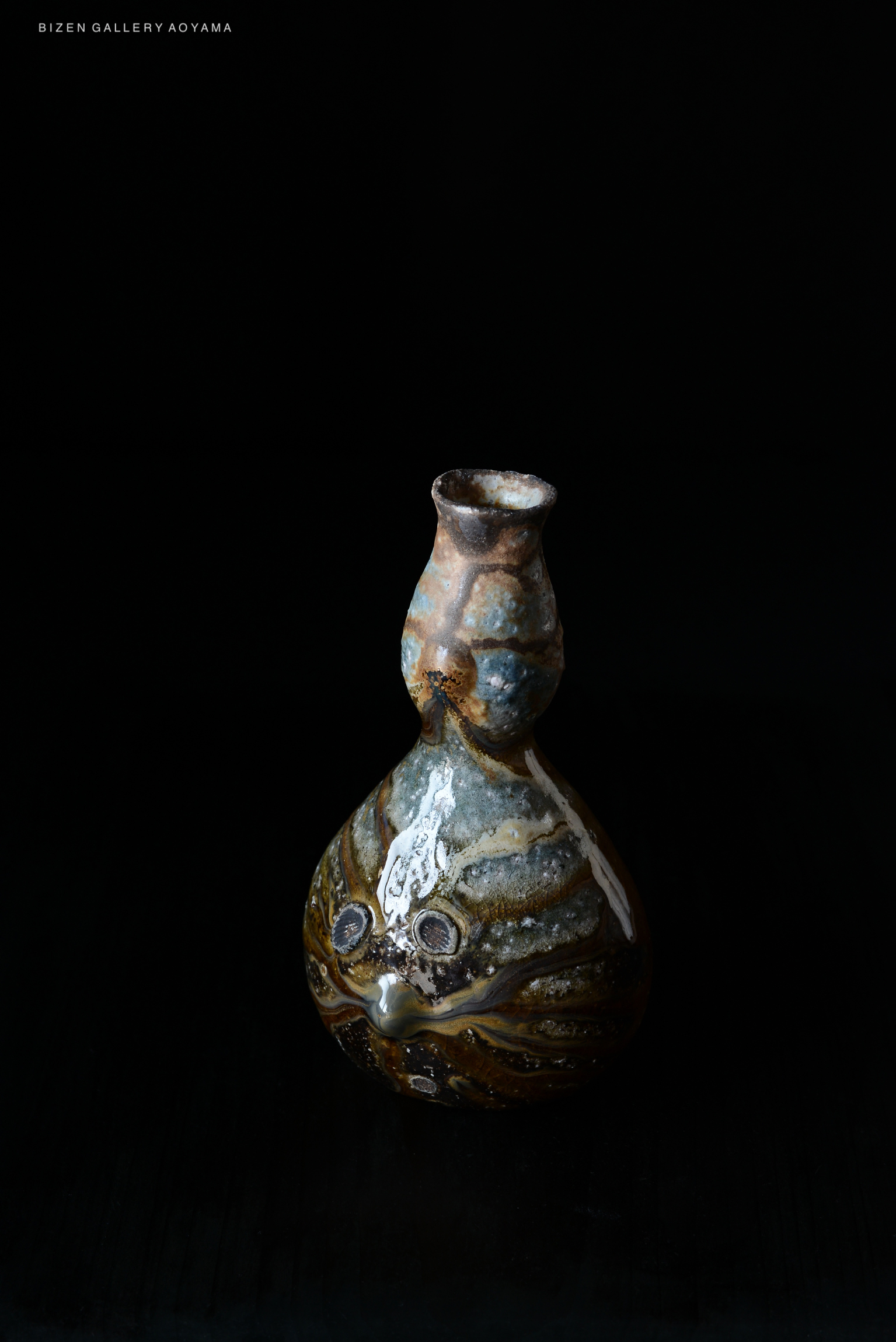 A decorative ceramic vase with a unique shape and textured surface, featuring blue and brown glazes, set against a black background.