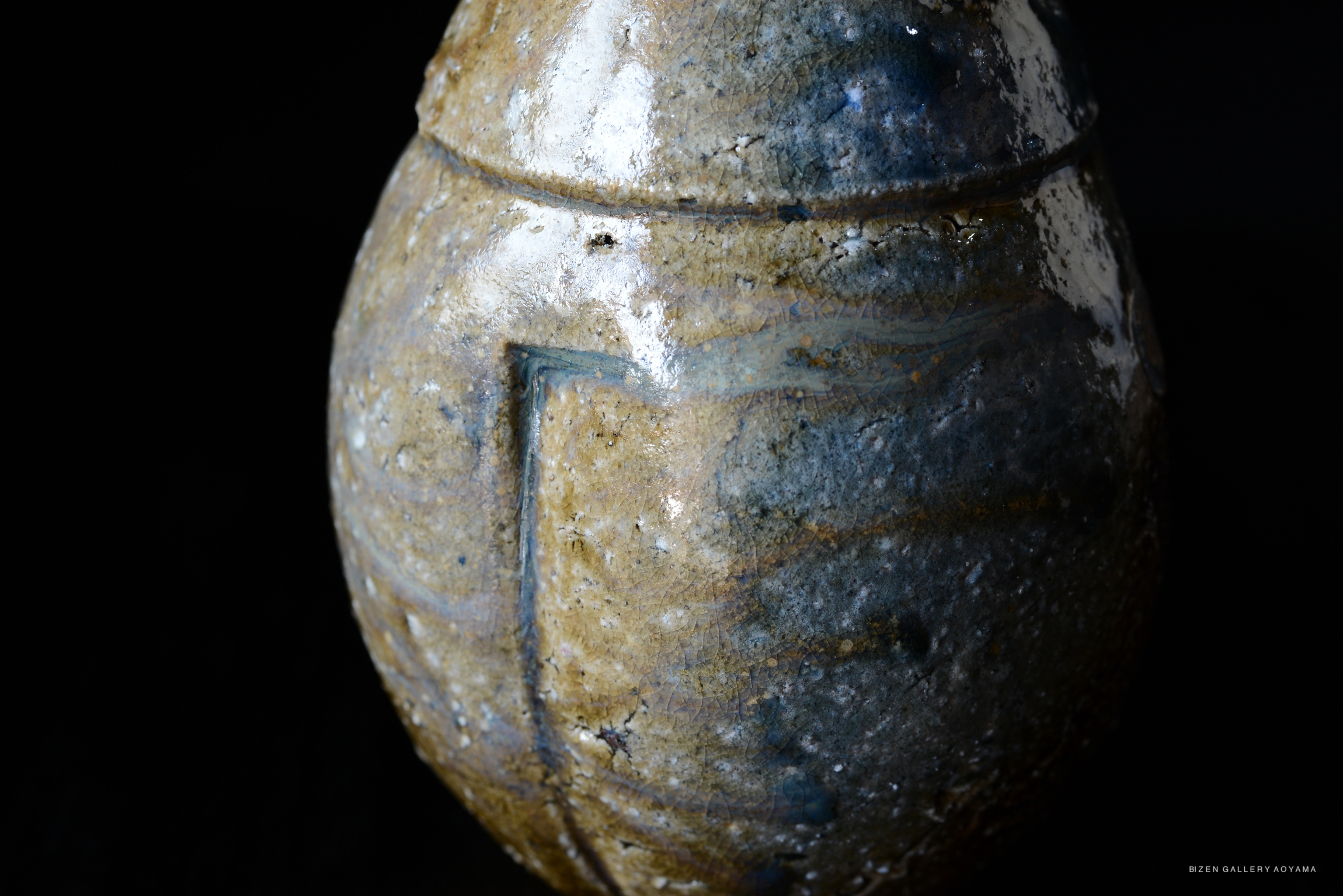 Close-up of a Bizen pottery vase showcasing a textured surface with blue and brown glazes against a dark background.