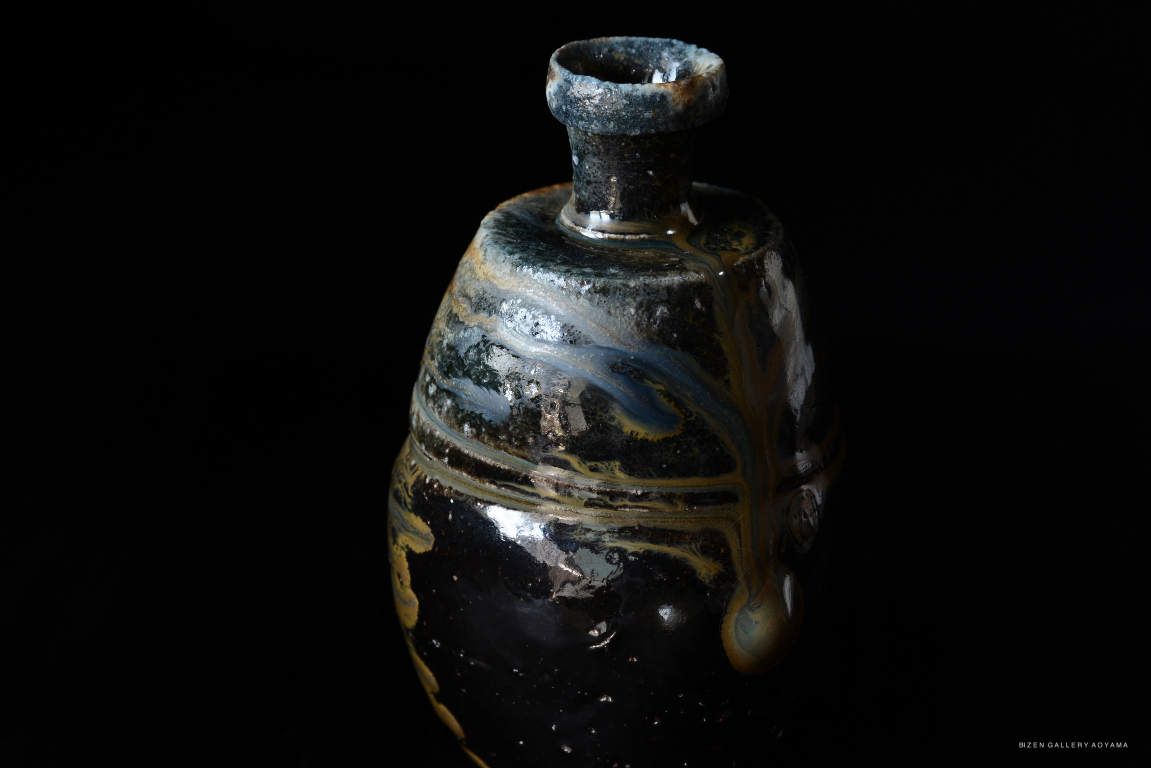 A close-up of a black and gold Japanese ceramic Tokkuri, showcasing its unique glaze patterns against a dark background.