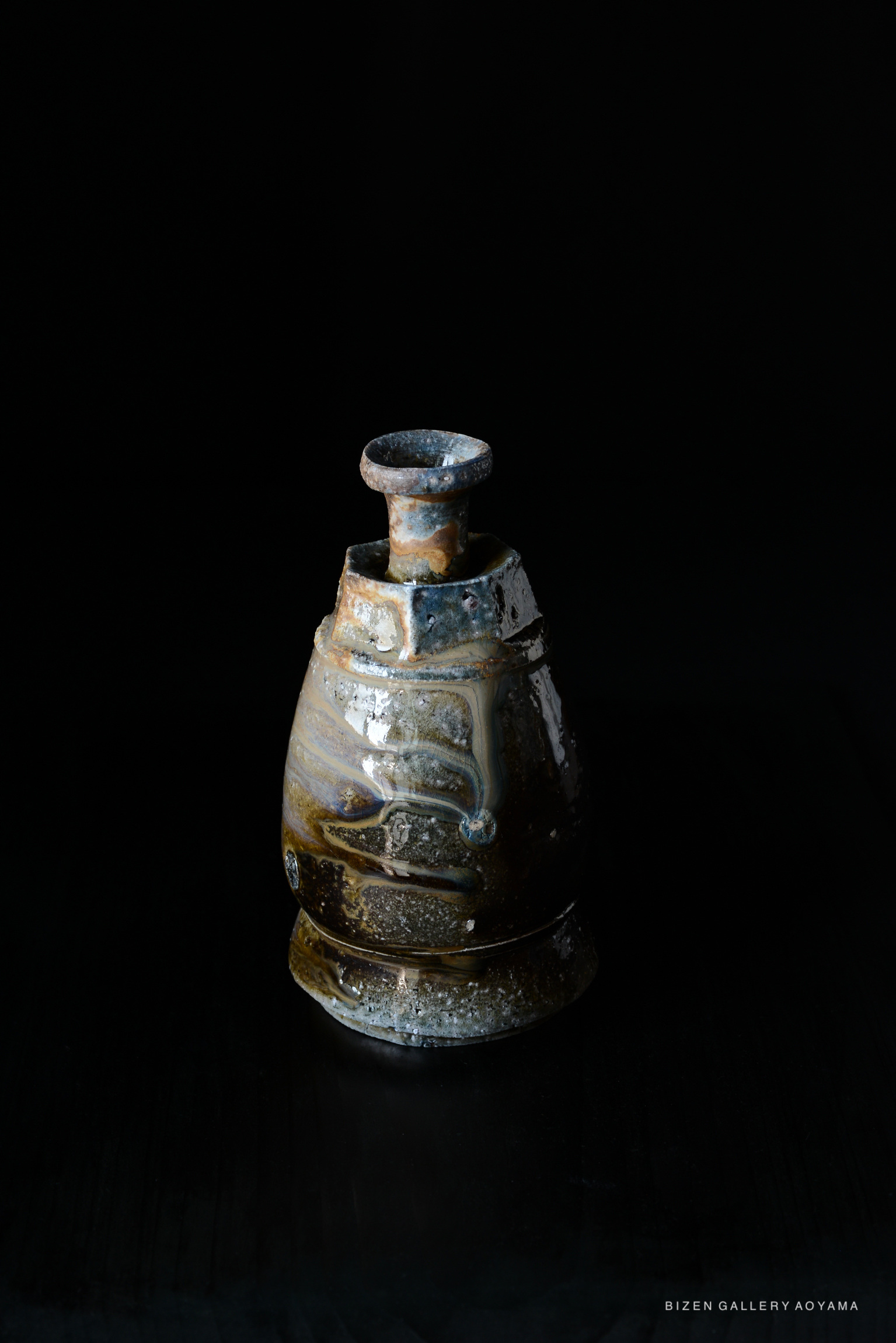 A traditional Japanese Kuro Tokkuri (black tokkuri) ceramic sake pot with a unique glaze finish, set against a dark background.