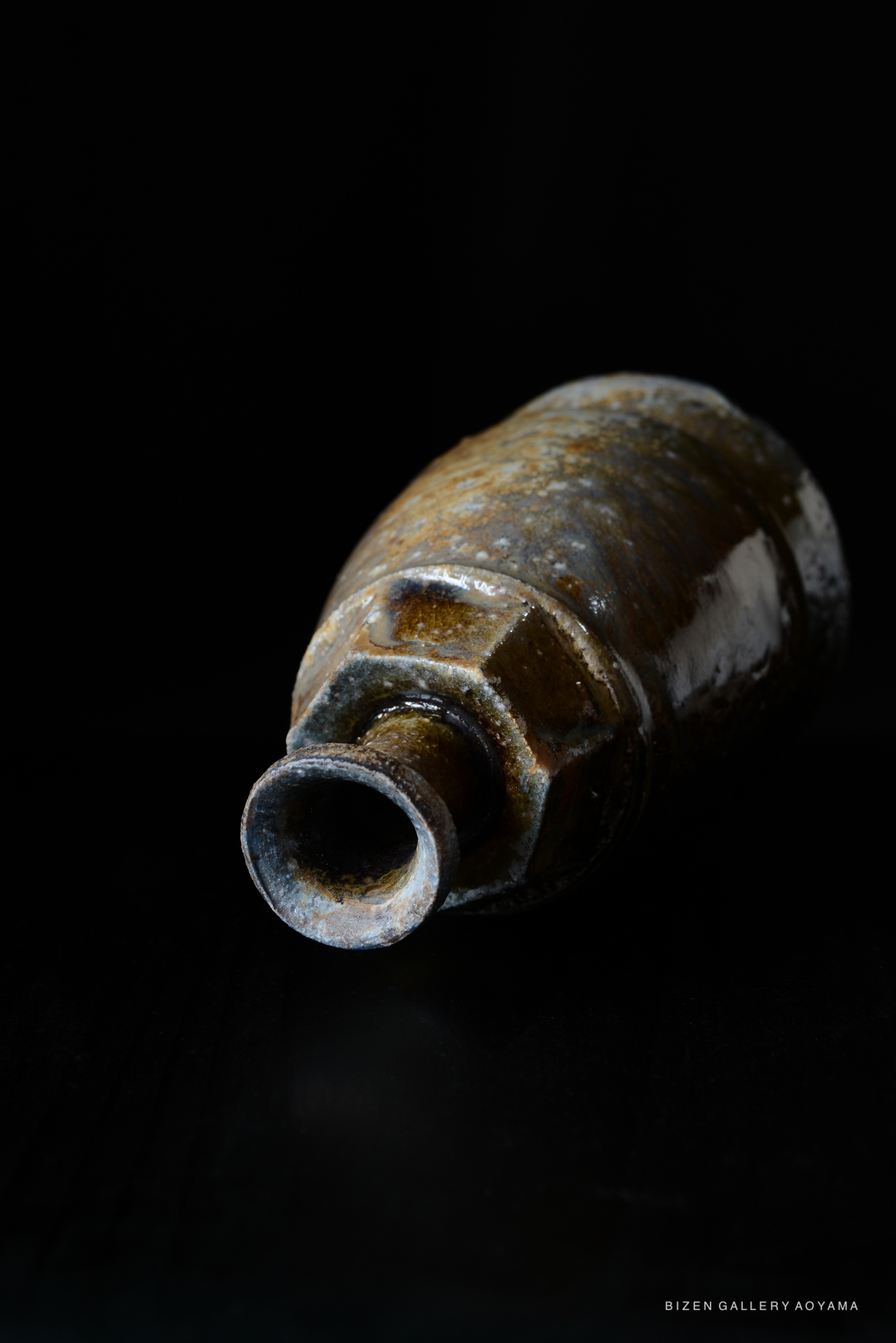 Close-up view of a traditional black Bizen pottery Tokkuri, showcasing its textured surface and unique shape against a dark background.