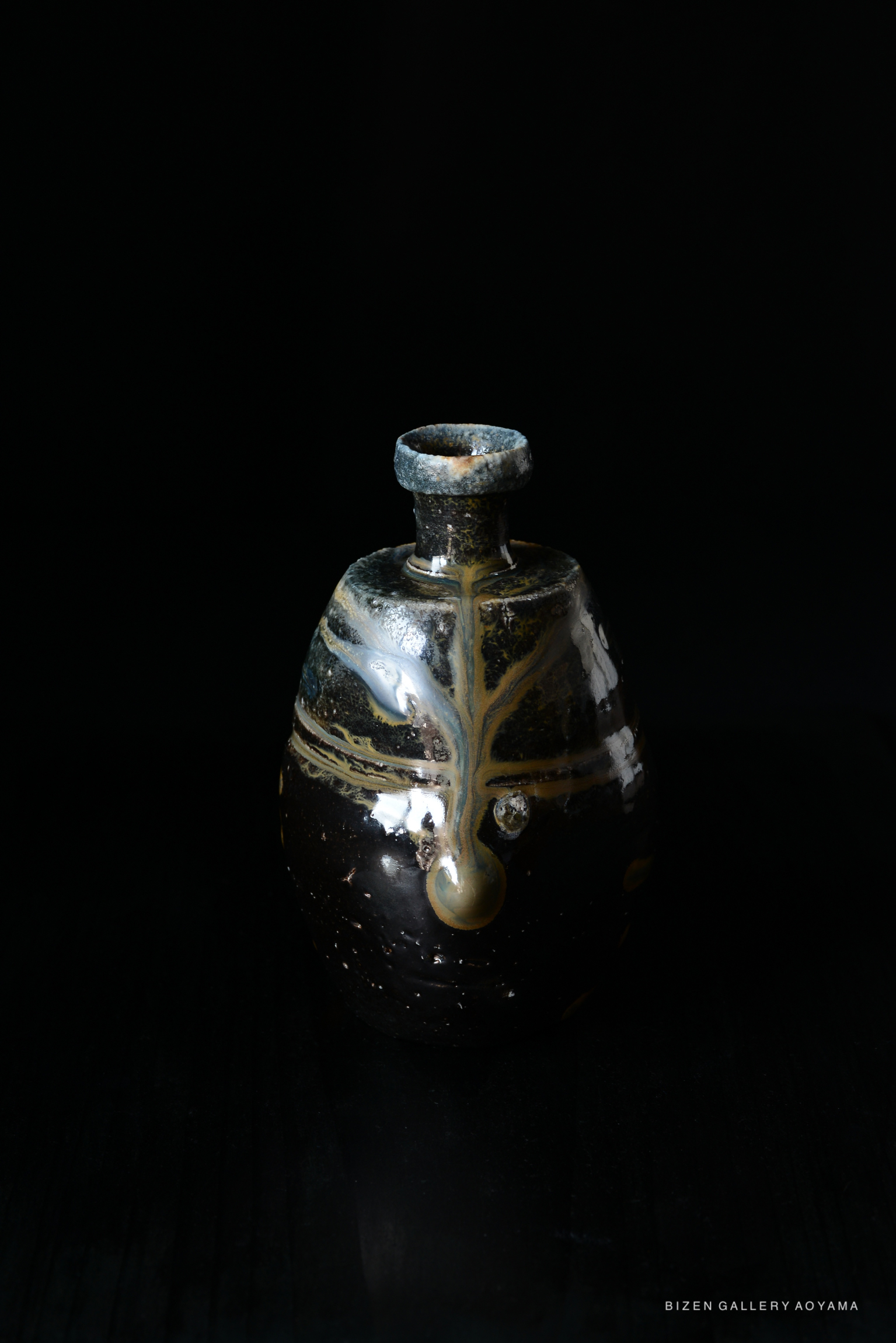 A traditional black Bizen pottery Tokkuri (sake flask) featuring a unique glaze with gold accents, displayed against a dark background.