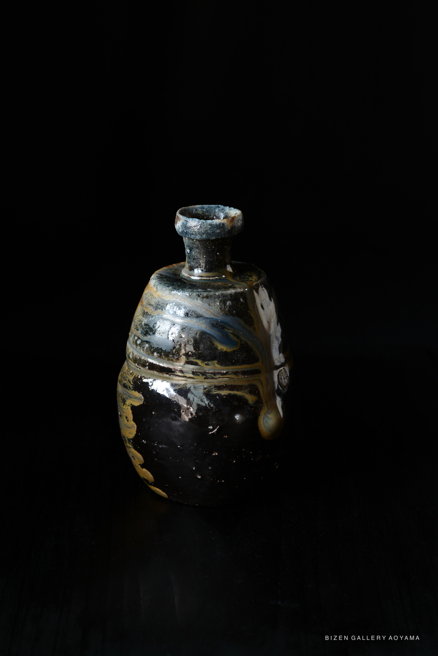 A Bizen pottery Tokkuri (sake bottle) with a unique design featuring dark tones and intricate patterns, set against a black backdrop.