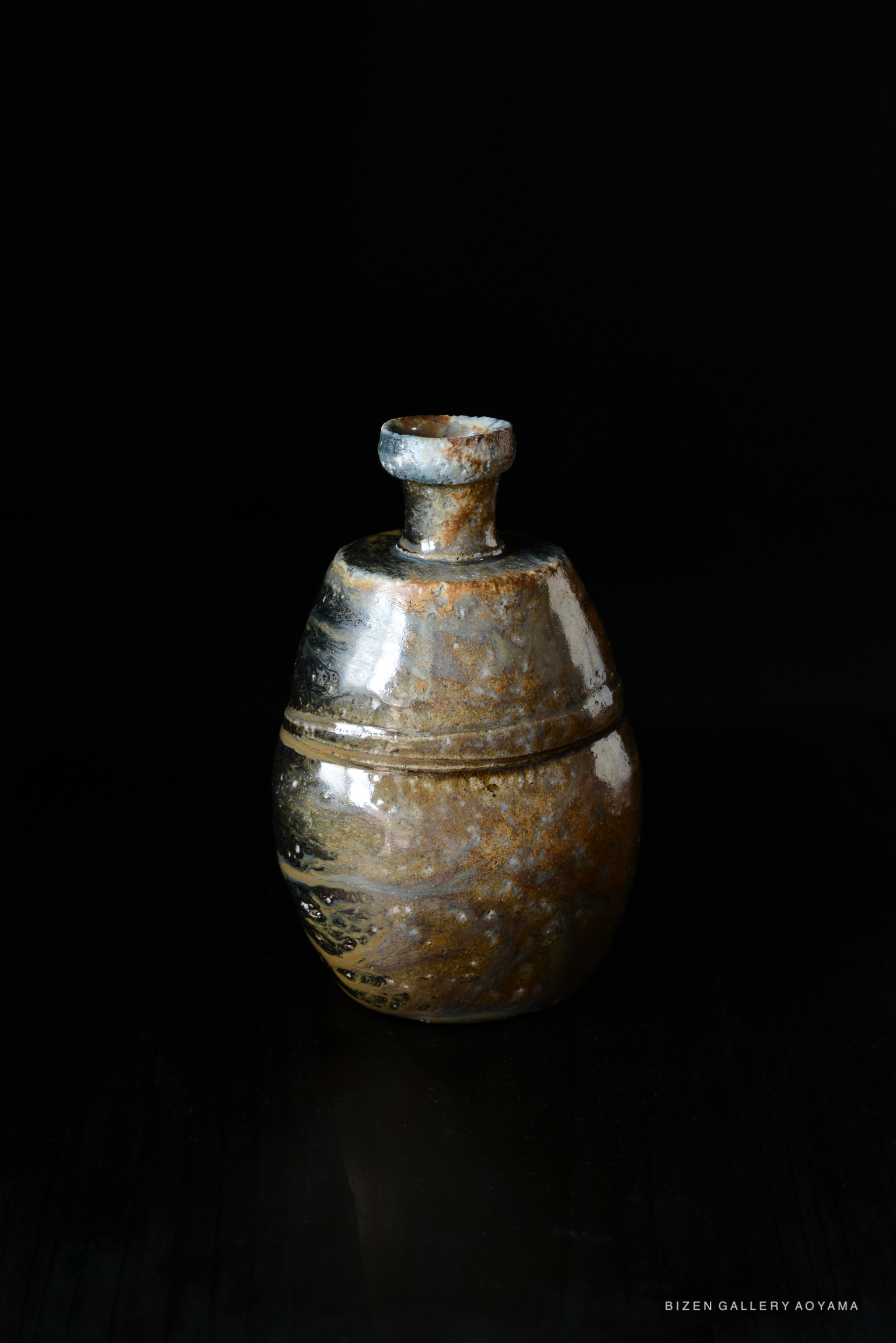 A traditional Japanese Kuro Tokkuri (black sake bottle) with a round body and narrow neck, showcasing earthy tones and a glossy finish, set against a dark background.