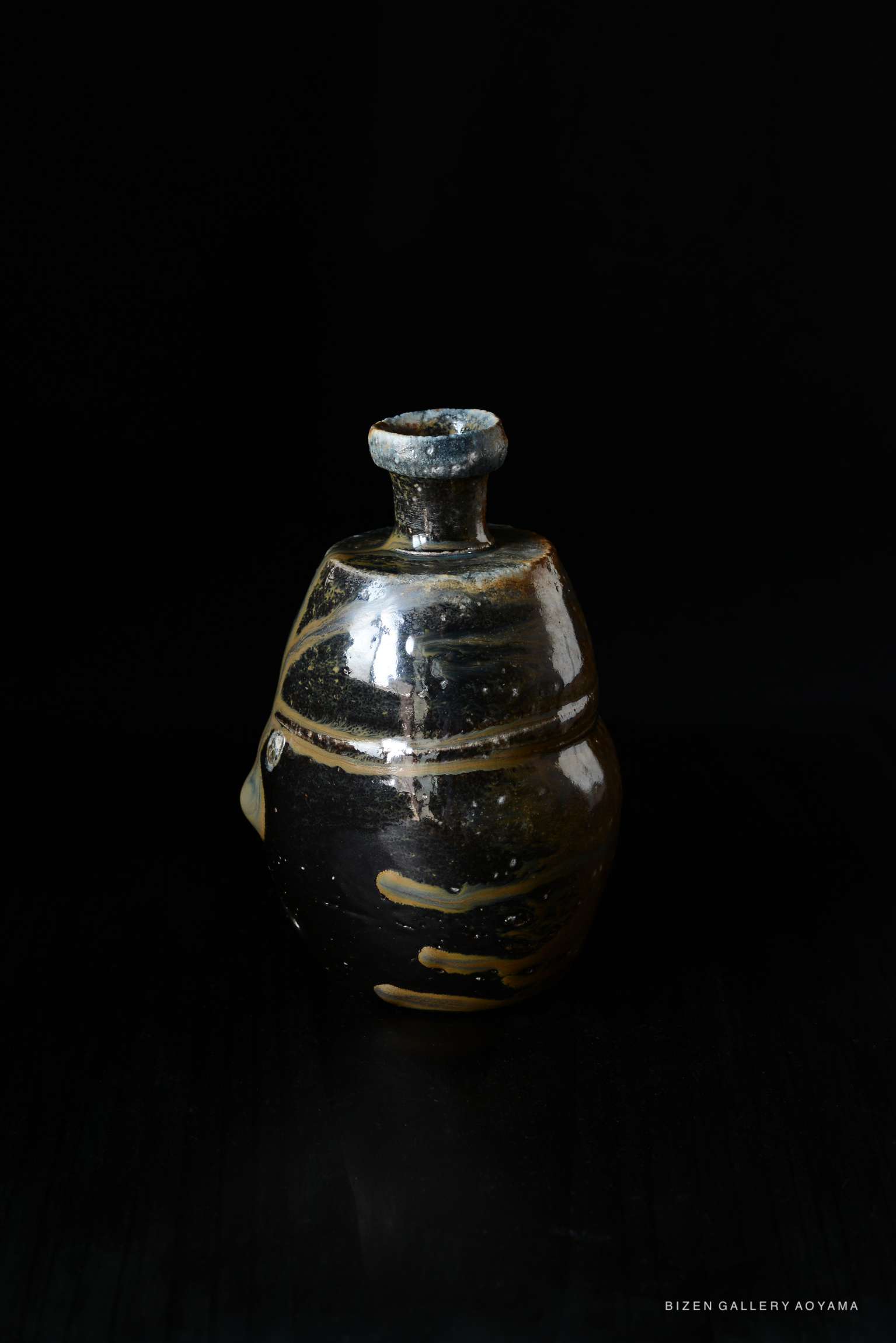 A black Bizen pottery Tokkuri, featuring a unique shape and glaze with earthy tones, set against a dark background.