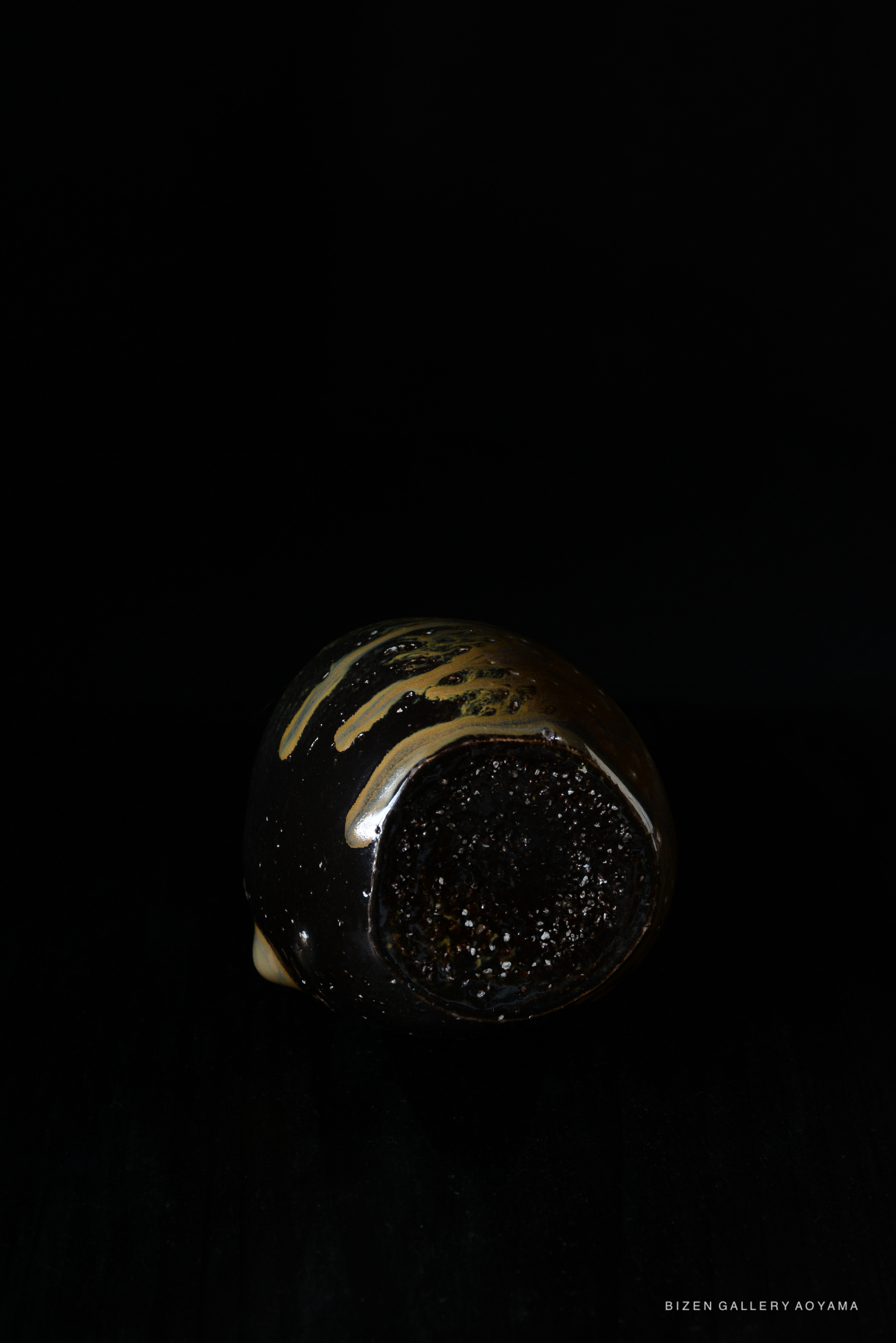 A close-up of a unique black ceramic vessel with a glossy surface and gold accents, showcased against a dark background.