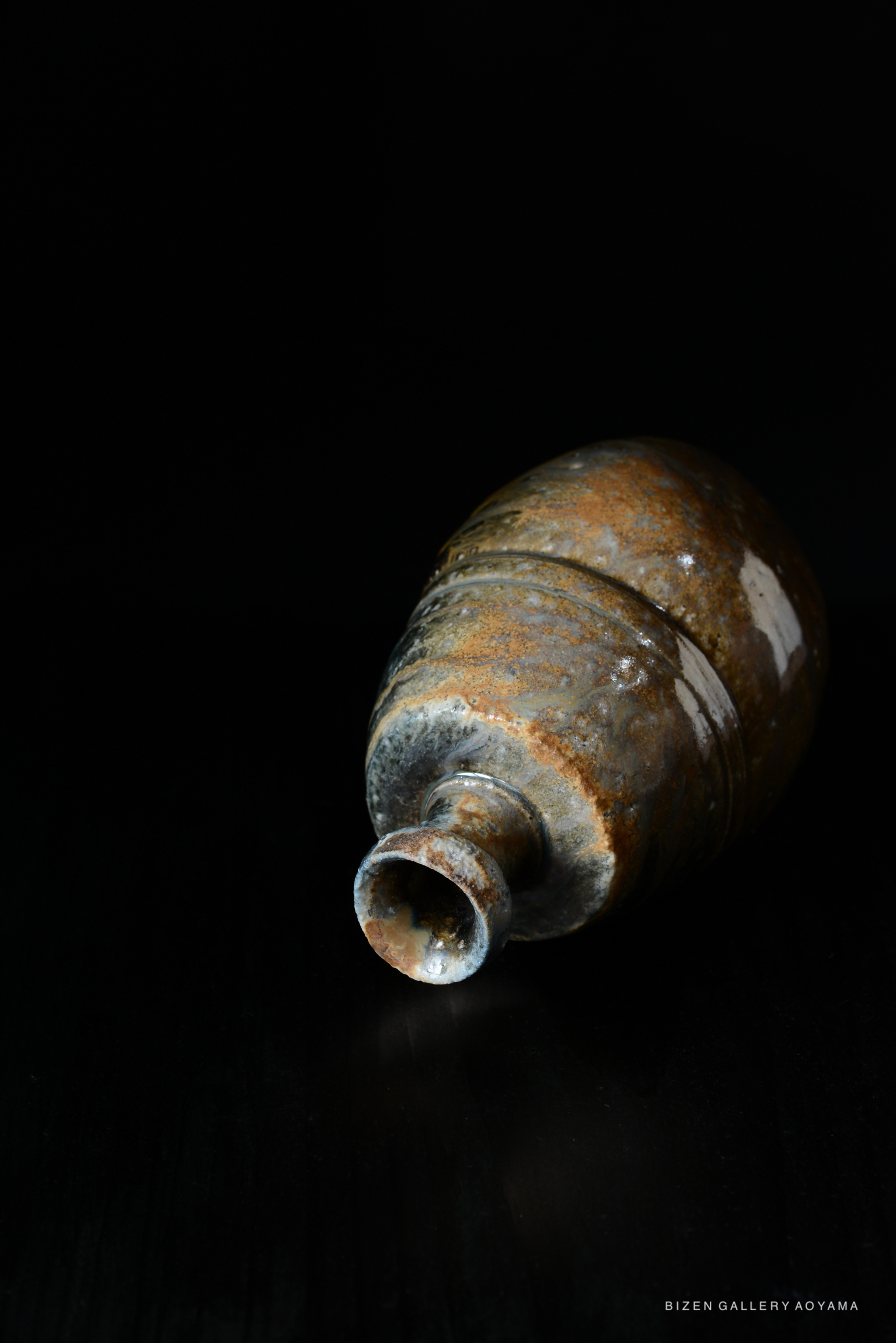 A close-up view of a traditional Japanese Tokkuri sake bottle, featuring earthy tones and a rustic texture, set against a dark background.
