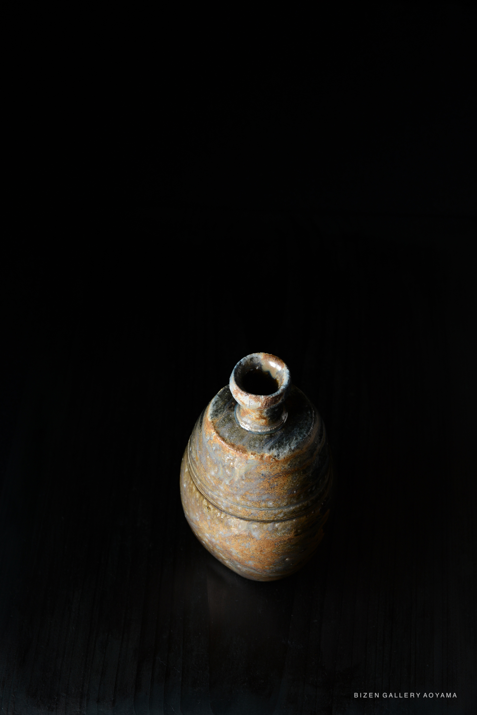A Bizen pottery Tokkuri (sake bottle) with an earthy texture, showcased against a black background.