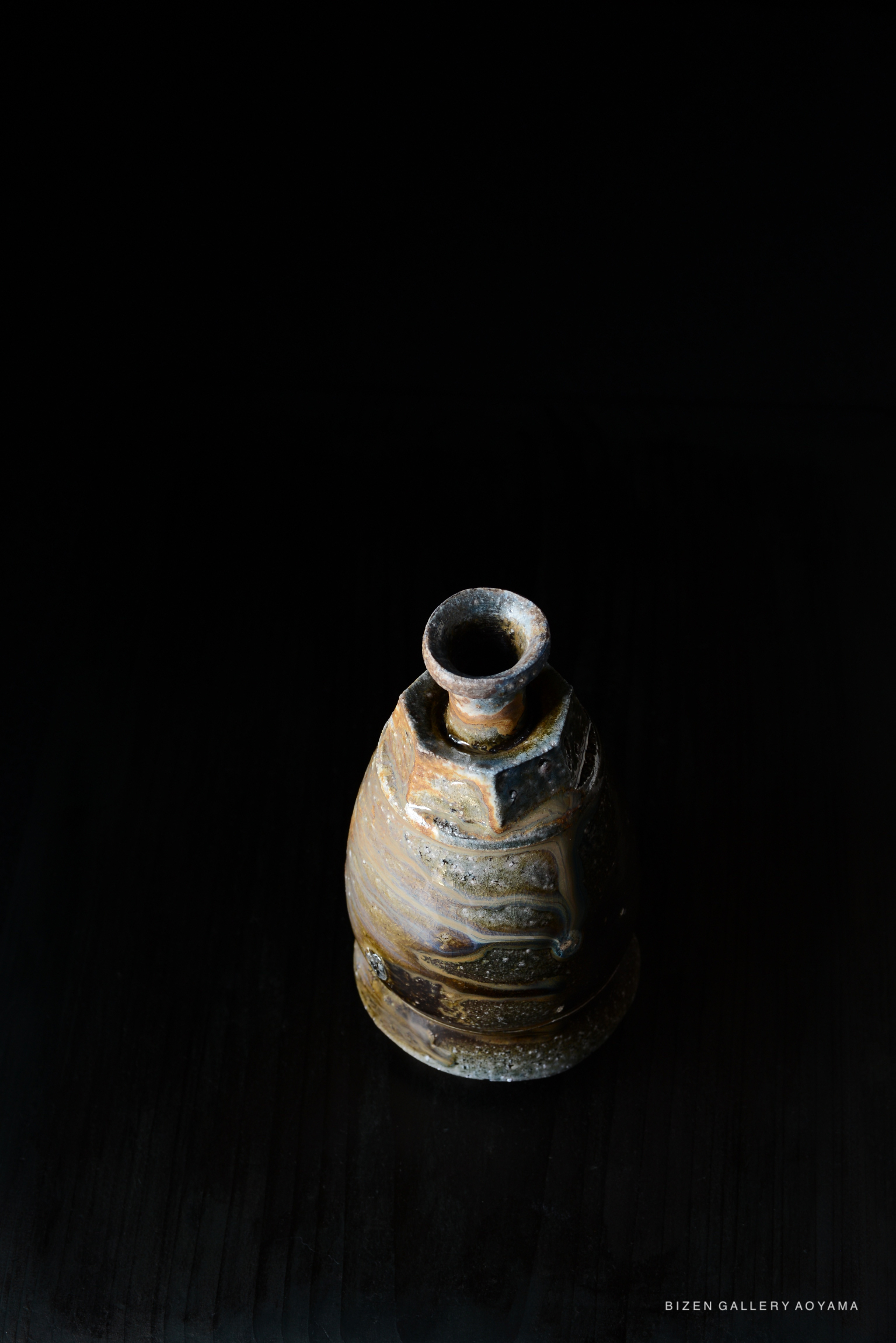 A handcrafted Bizen pottery tokkuri (sake server) with a unique glaze pattern, set against a dark background.