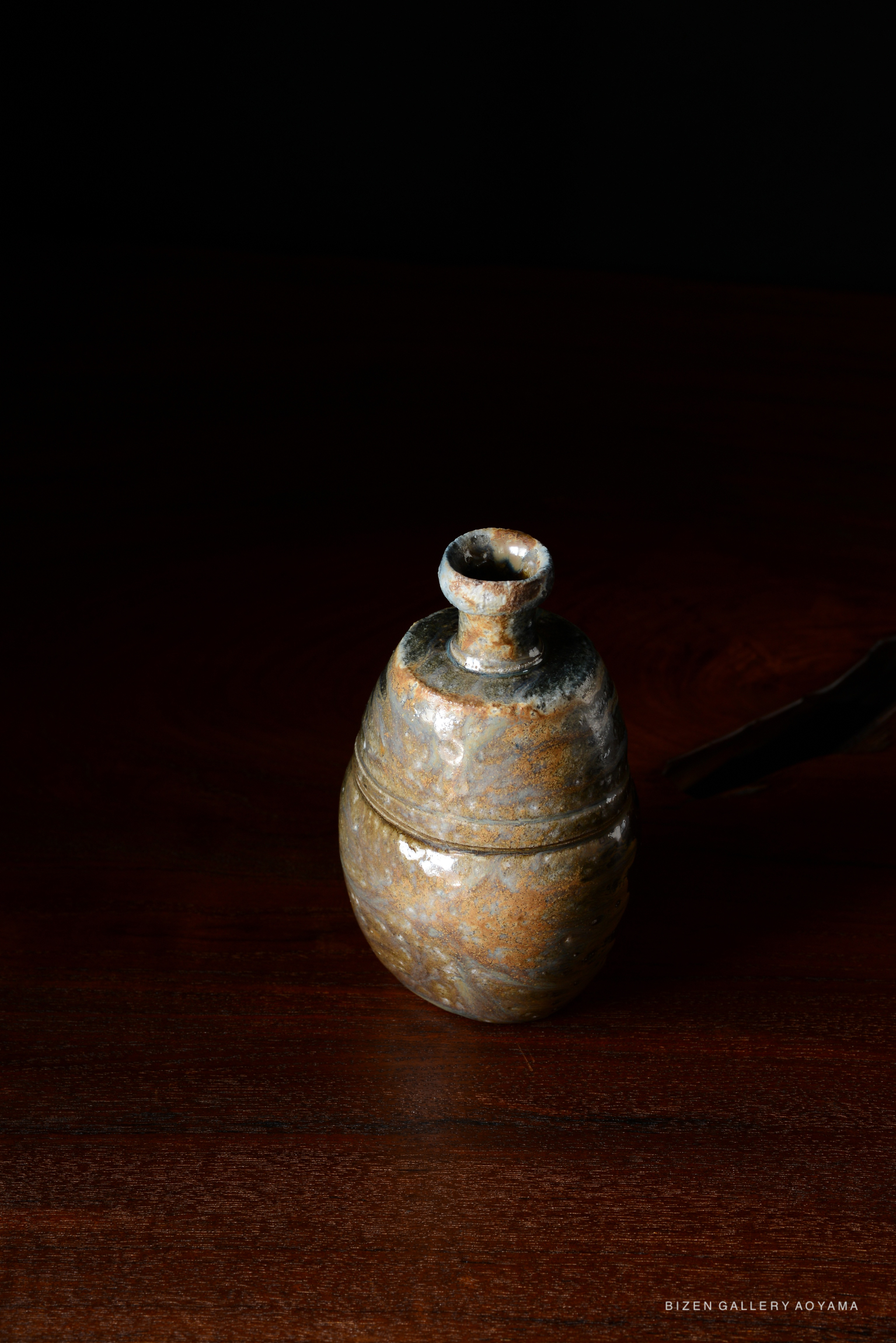 A traditional Japanese Kuro Tokkuri (black sake bottle) with a rounded body and narrow neck, displayed on a wooden surface against a dark background.
