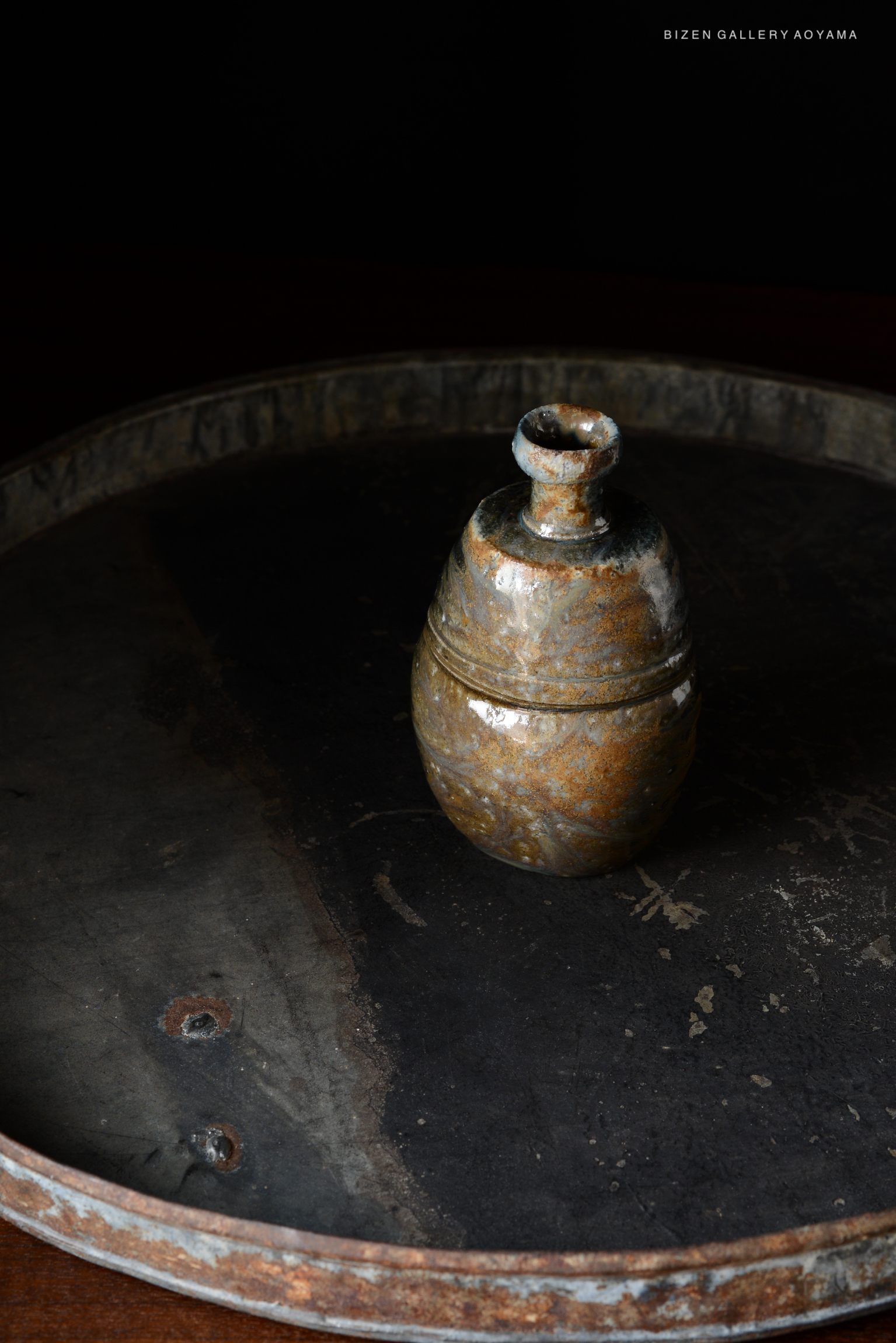 An antique Kuro Tokkuri (black sake bottle) placed on a round, dark surface, showcasing earthy tones and rustic texture.