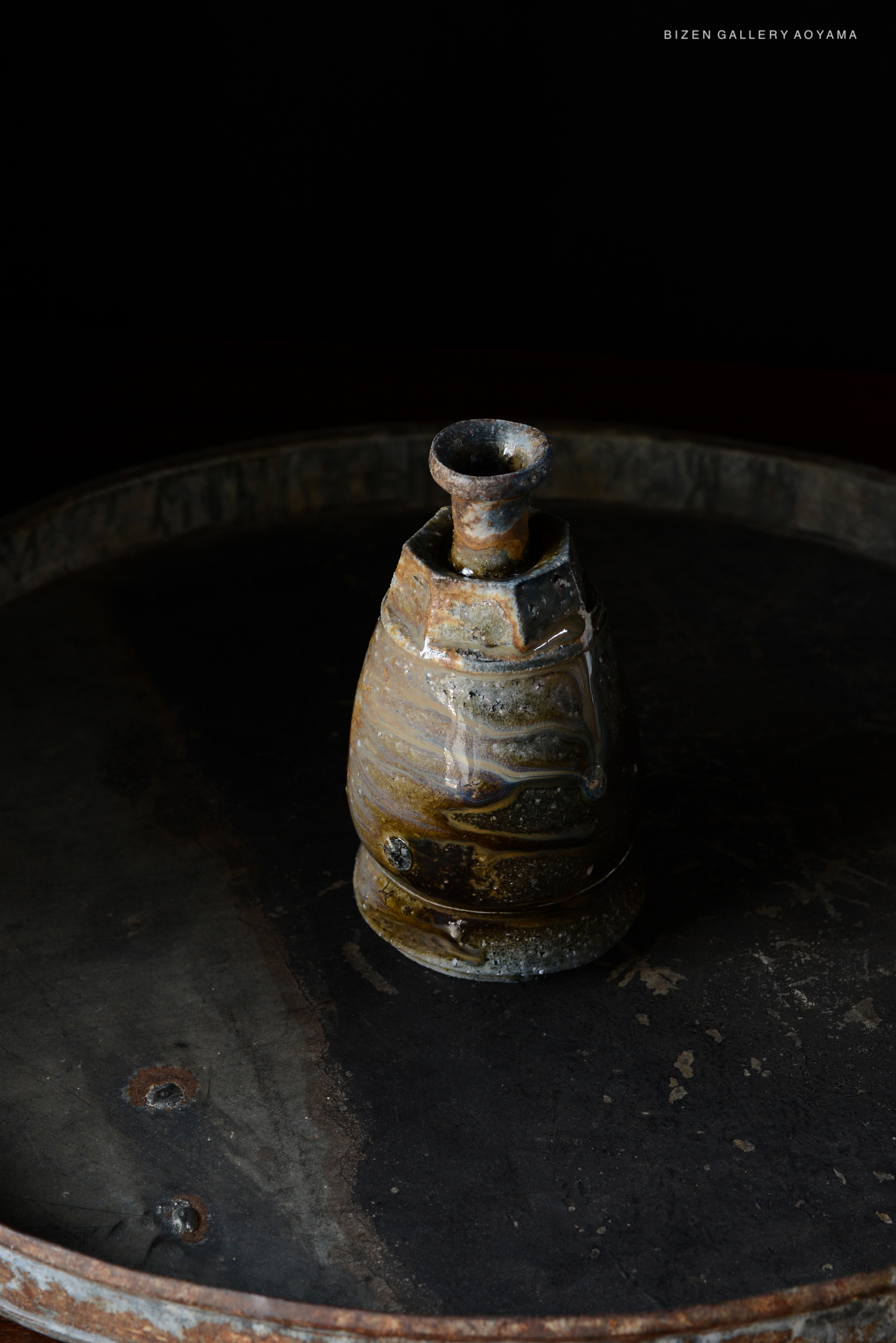 A close-up of a traditional Bizen pottery Tokkuri, featuring a unique glaze and texture, displayed on a dark surface.