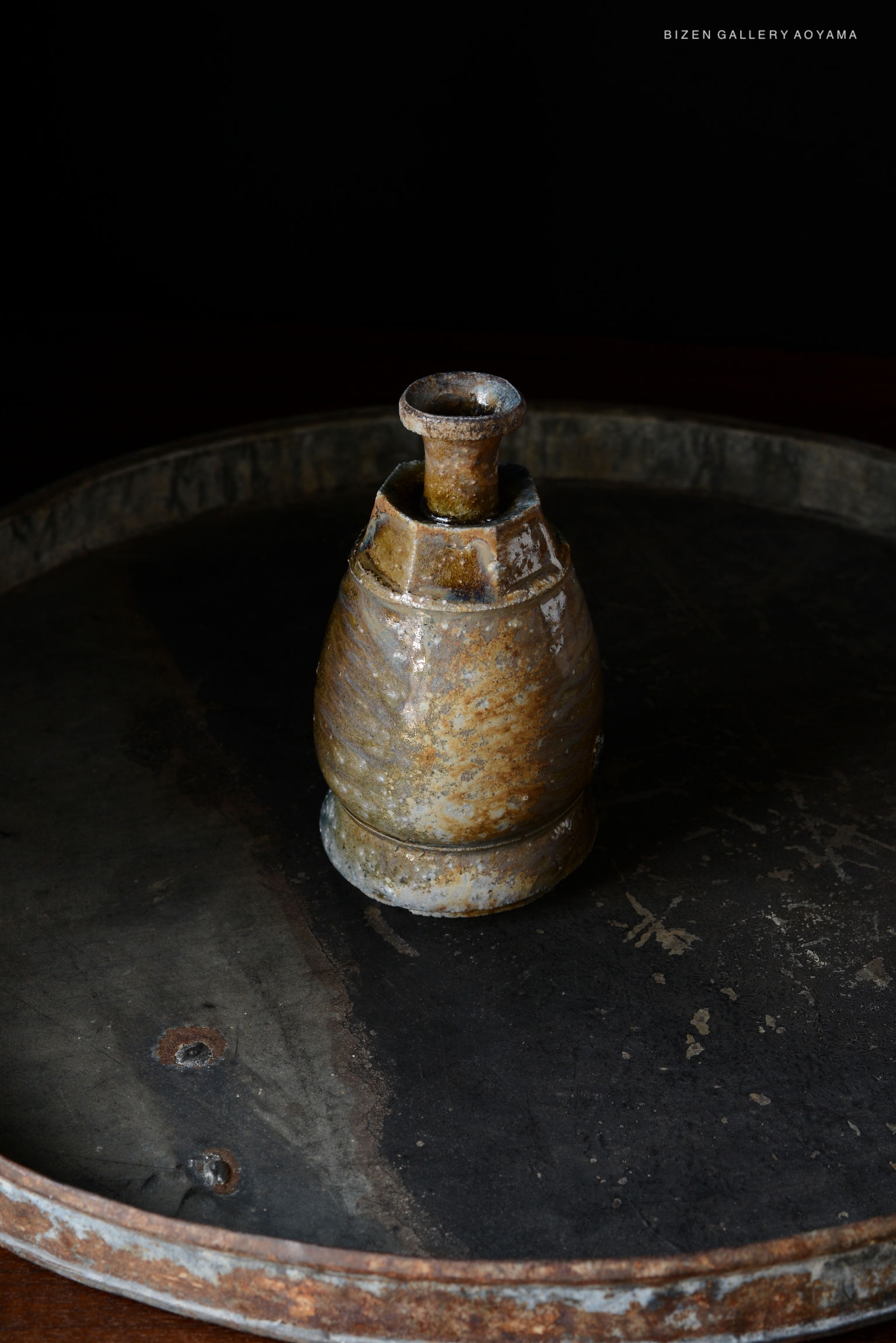 A traditional Japanese Kuro Tokkuri, a sake pitcher, displayed on a rustic circular tray against a dark background.
