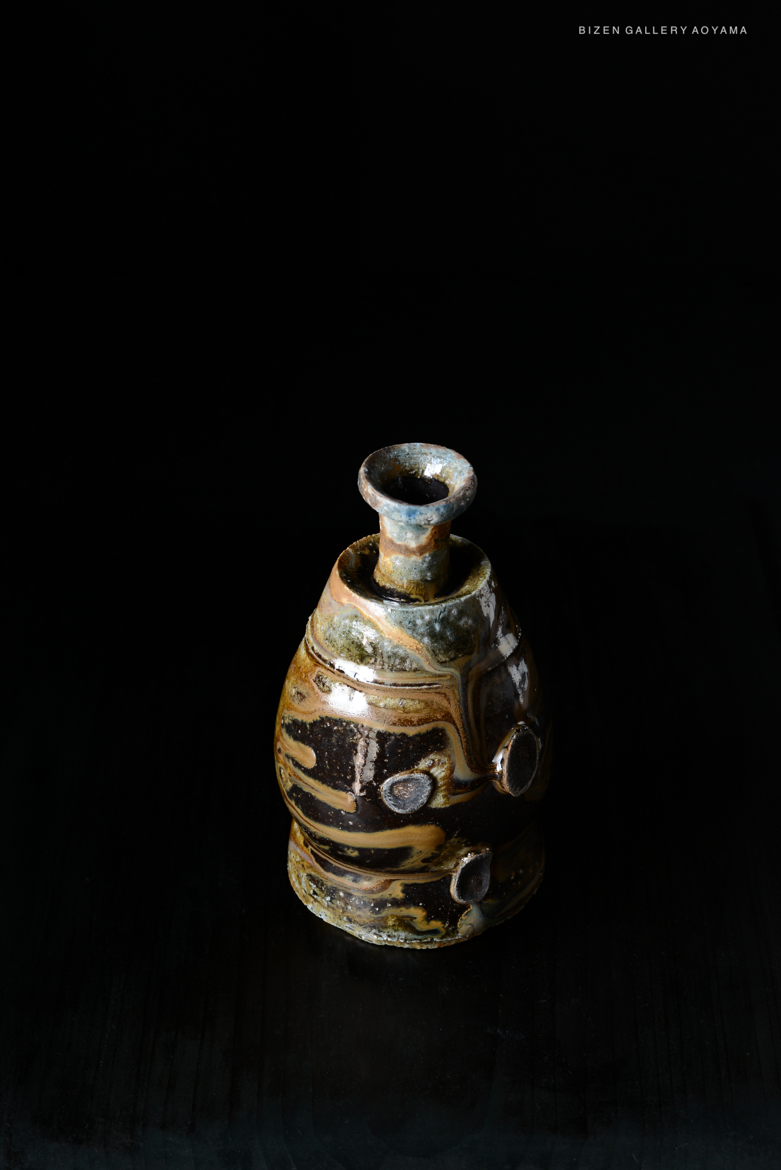 A close-up view of a traditional black Bizen pottery Tokkuri (sake flask) with unique glazing patterns, set against a dark background.