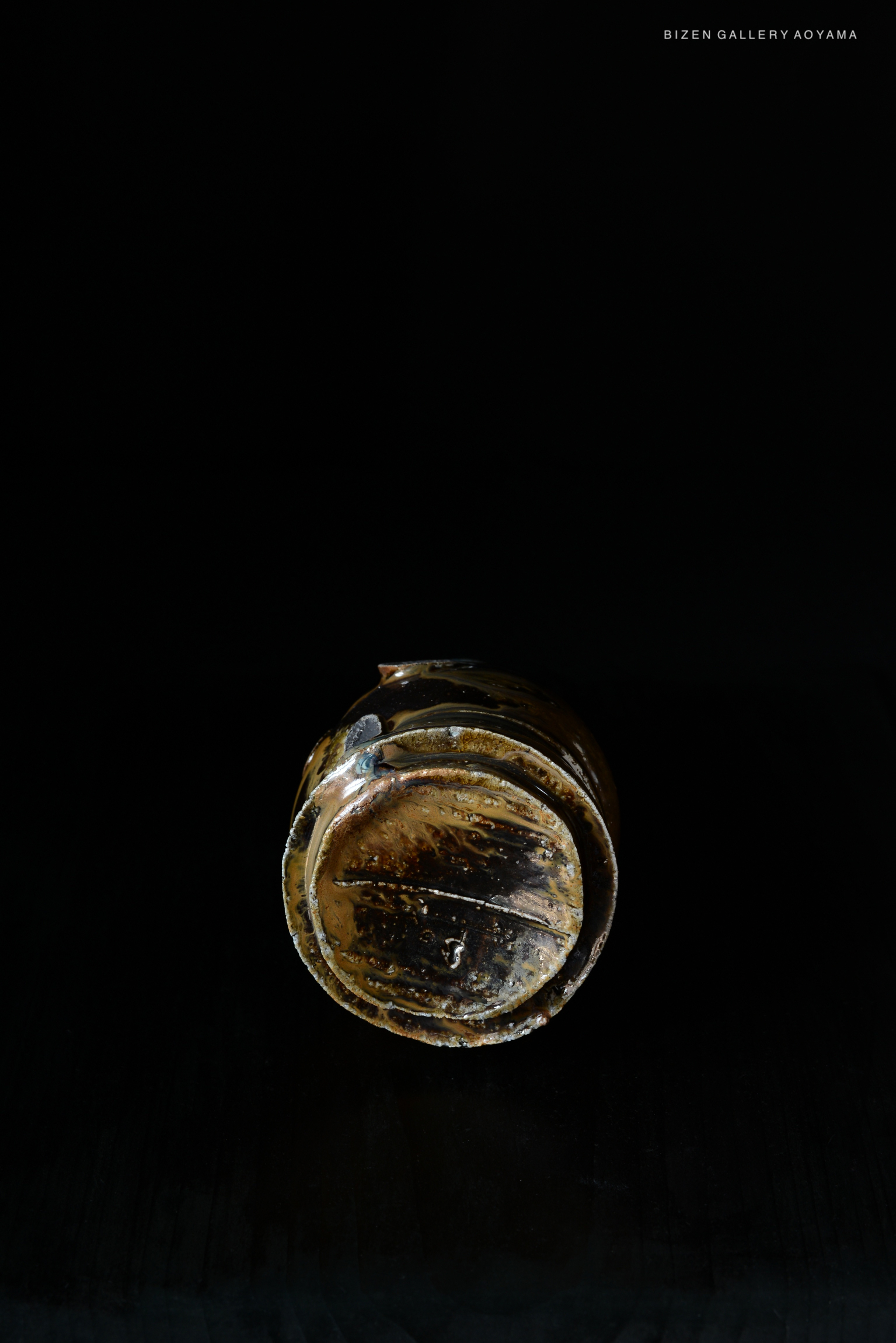 A close-up view of a Kuro Tokkuri, a traditional Japanese sake vessel, showcasing its distinctive dark, textured surface against a black background.