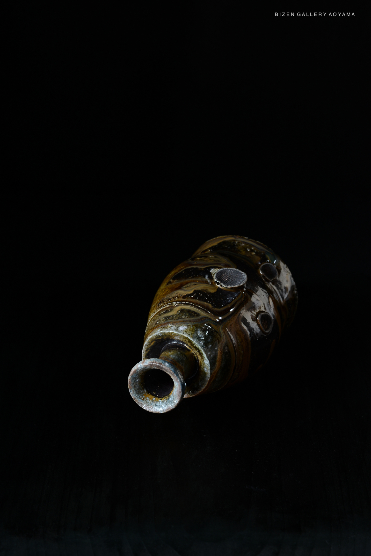 A close-up image of a traditional Kuro Tokkuri (black sake bottle) with organic shapes and dark glaze, set against a black background.
