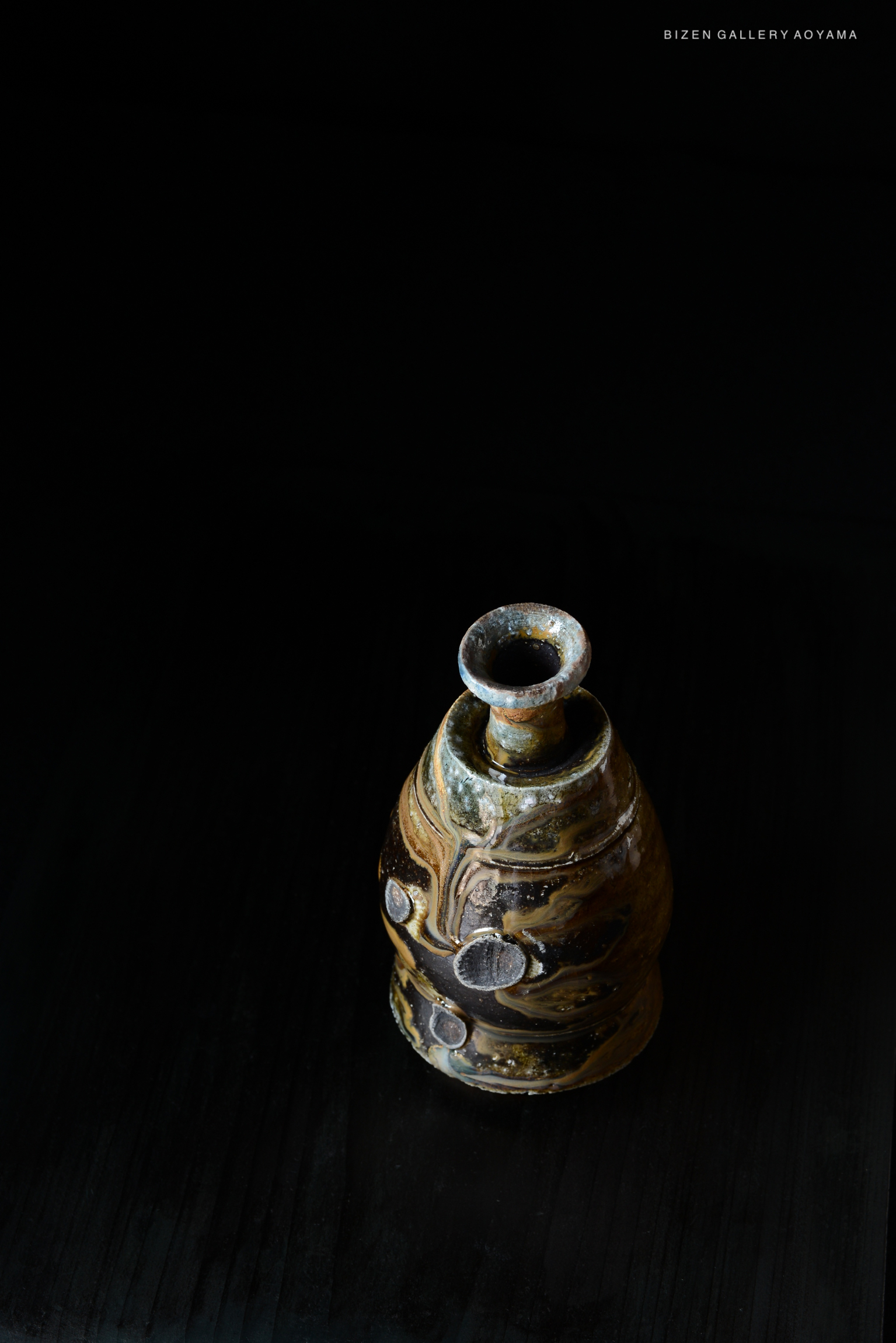 A unique ceramic sake vessel, known as Kuro Tokkuri, displayed against a dark background. The vessel has a distinct shape with textured patterns and variations in color, showcasing the artistry of Bizen pottery.