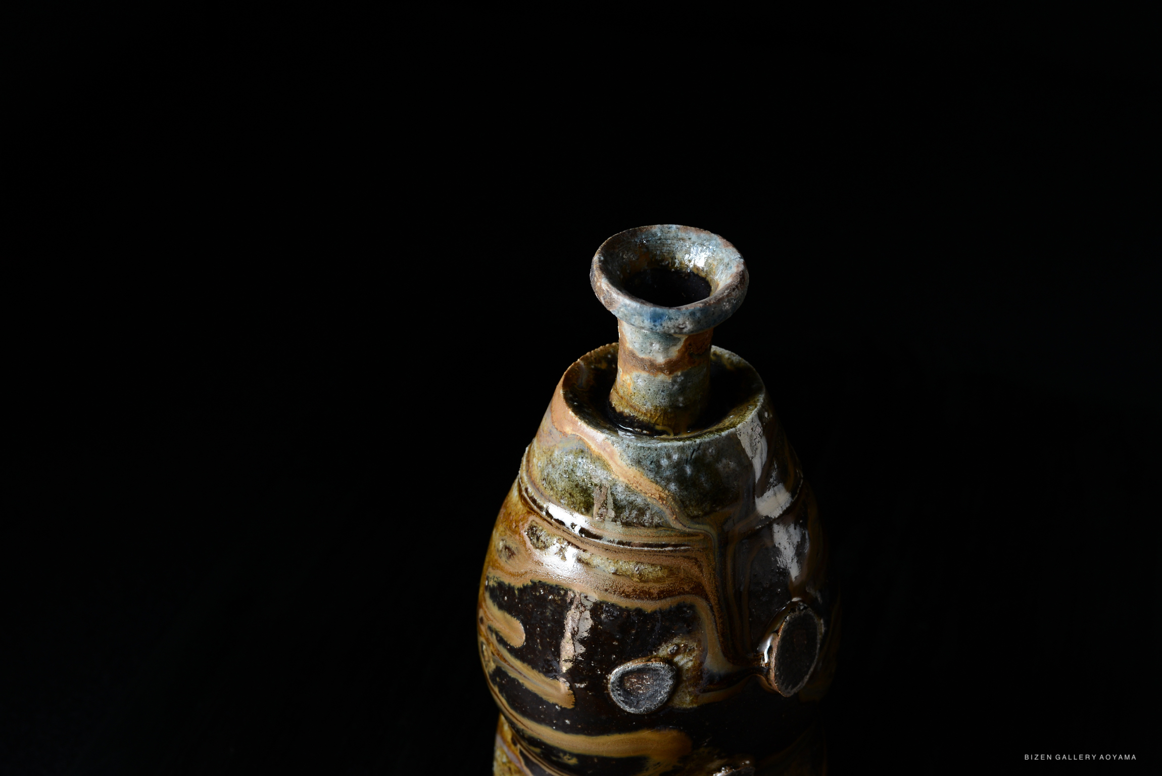 A close-up view of a Kuro Tokkuri, a traditional Japanese sake bottle, featuring a unique glazes and textures against a black background.
