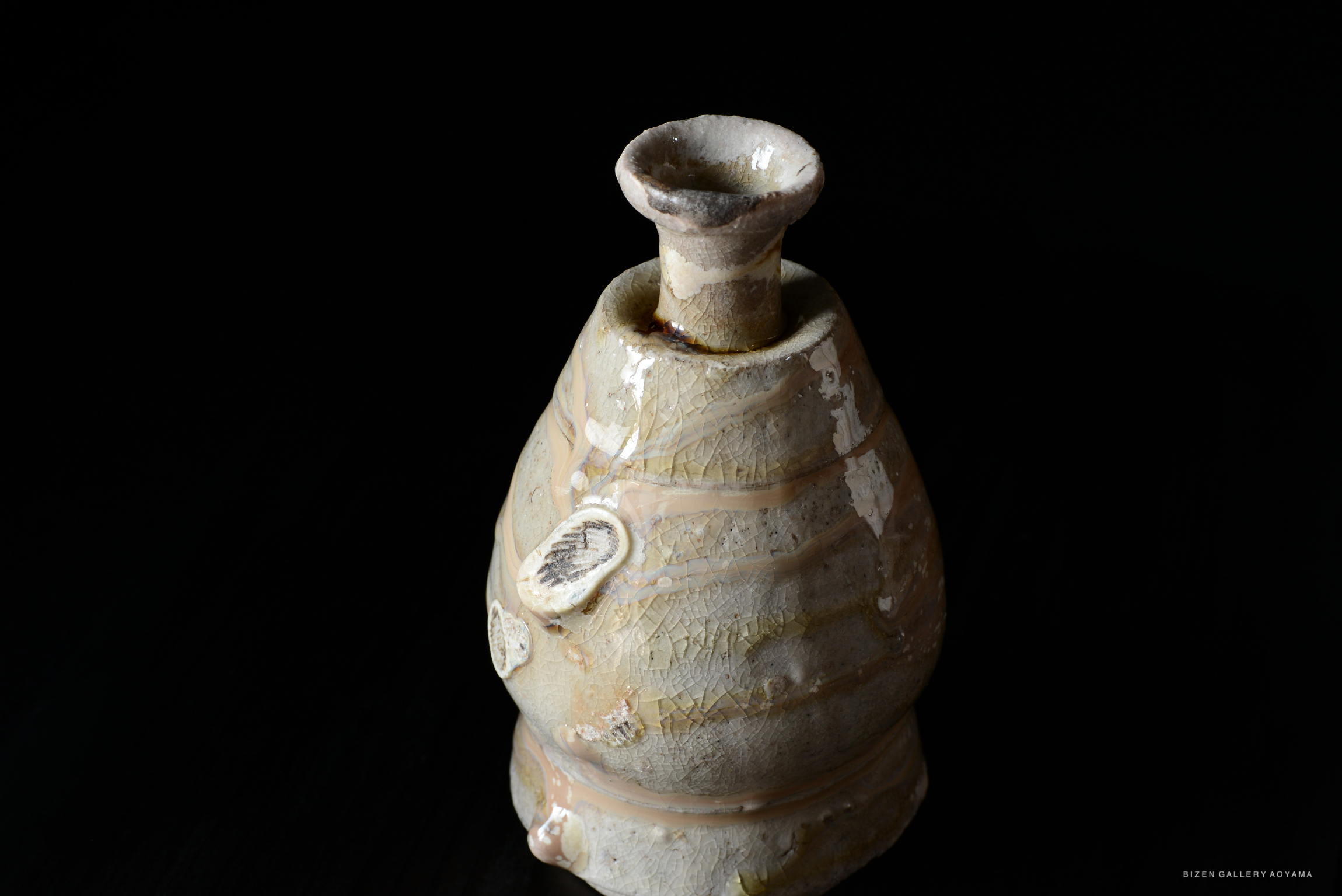 Ceramic shiro tokkuri (sake bottle) with a textured surface and subtle colors, set against a dark background.