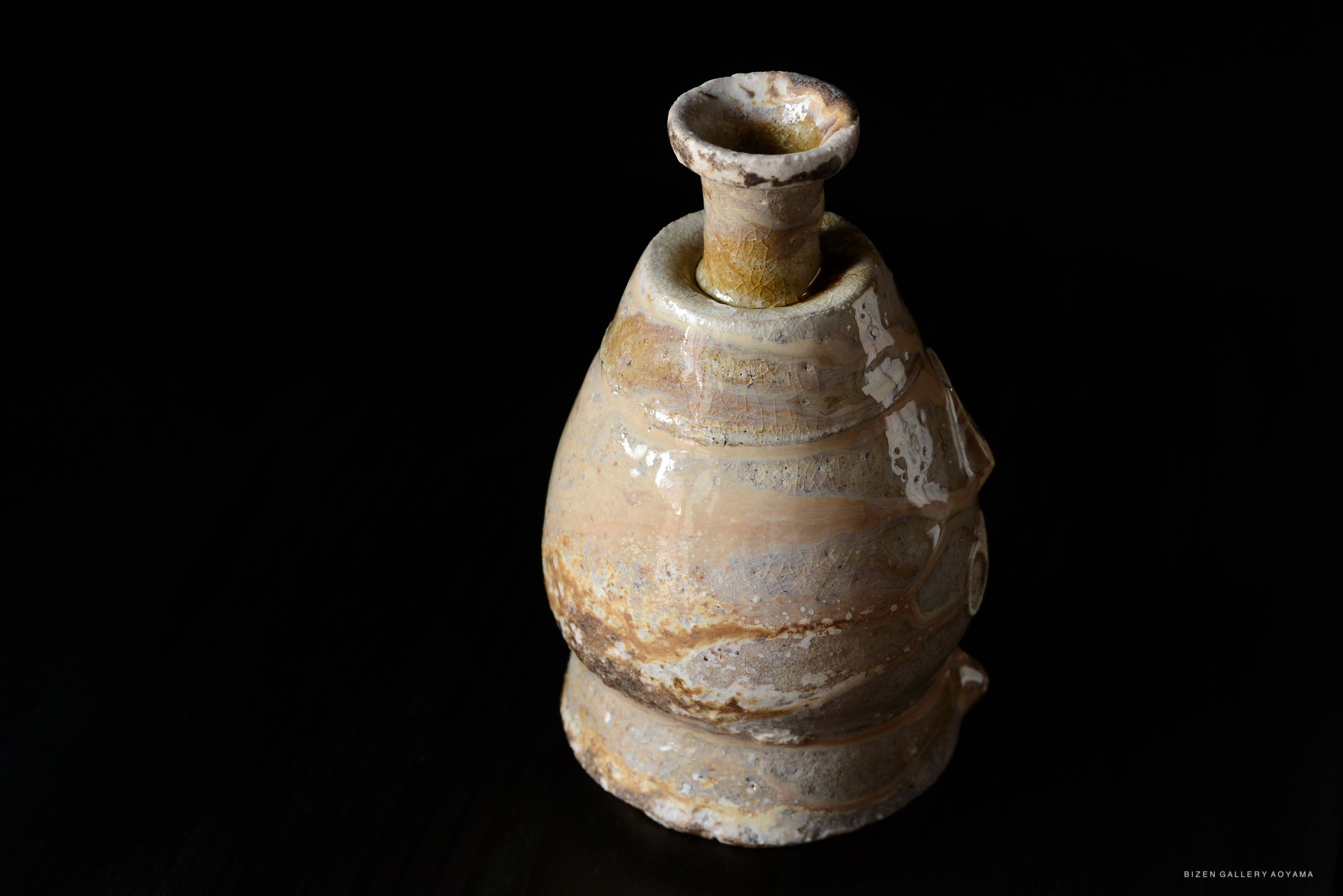 A rustic Bizen pottery shiro tokkuri, featuring a unique, earthy glaze and an elegant, curvy shape, set against a dark background.