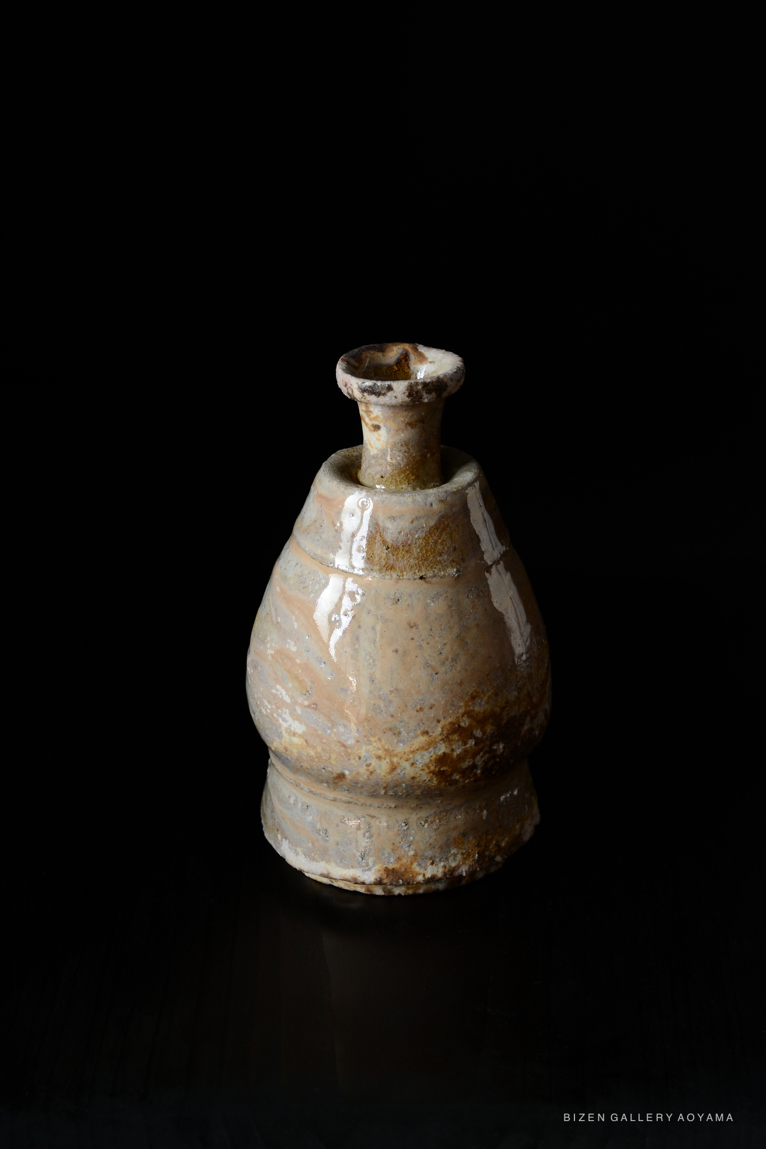 A traditional Bizen pottery shiro tokkuri, featuring a rounded body and a narrow neck, displayed on a dark background.