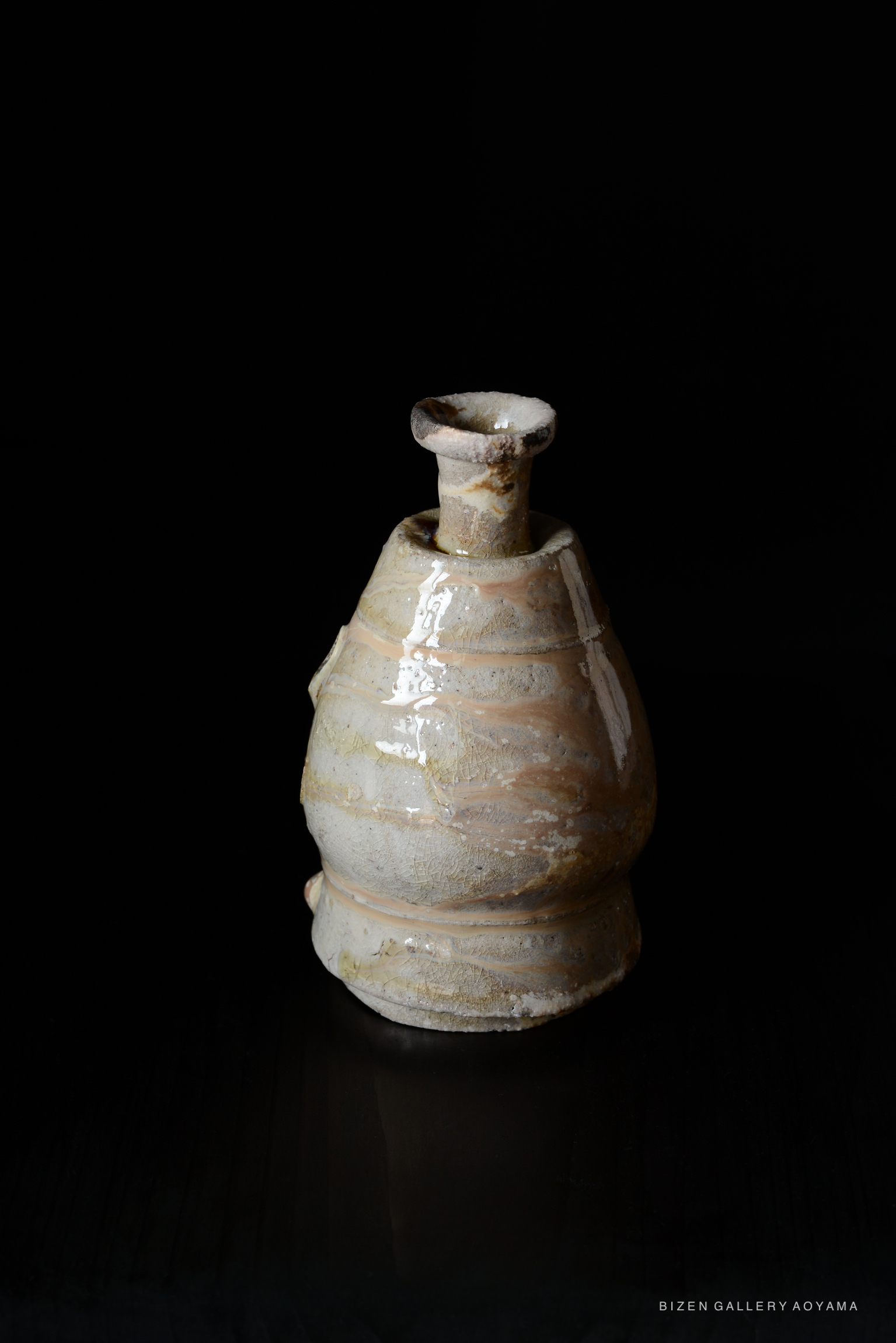 A traditional Shiro Tokkuri sake vessel made of Bizen pottery, featuring a unique swirled texture and a neutral color palette, displayed against a black background.