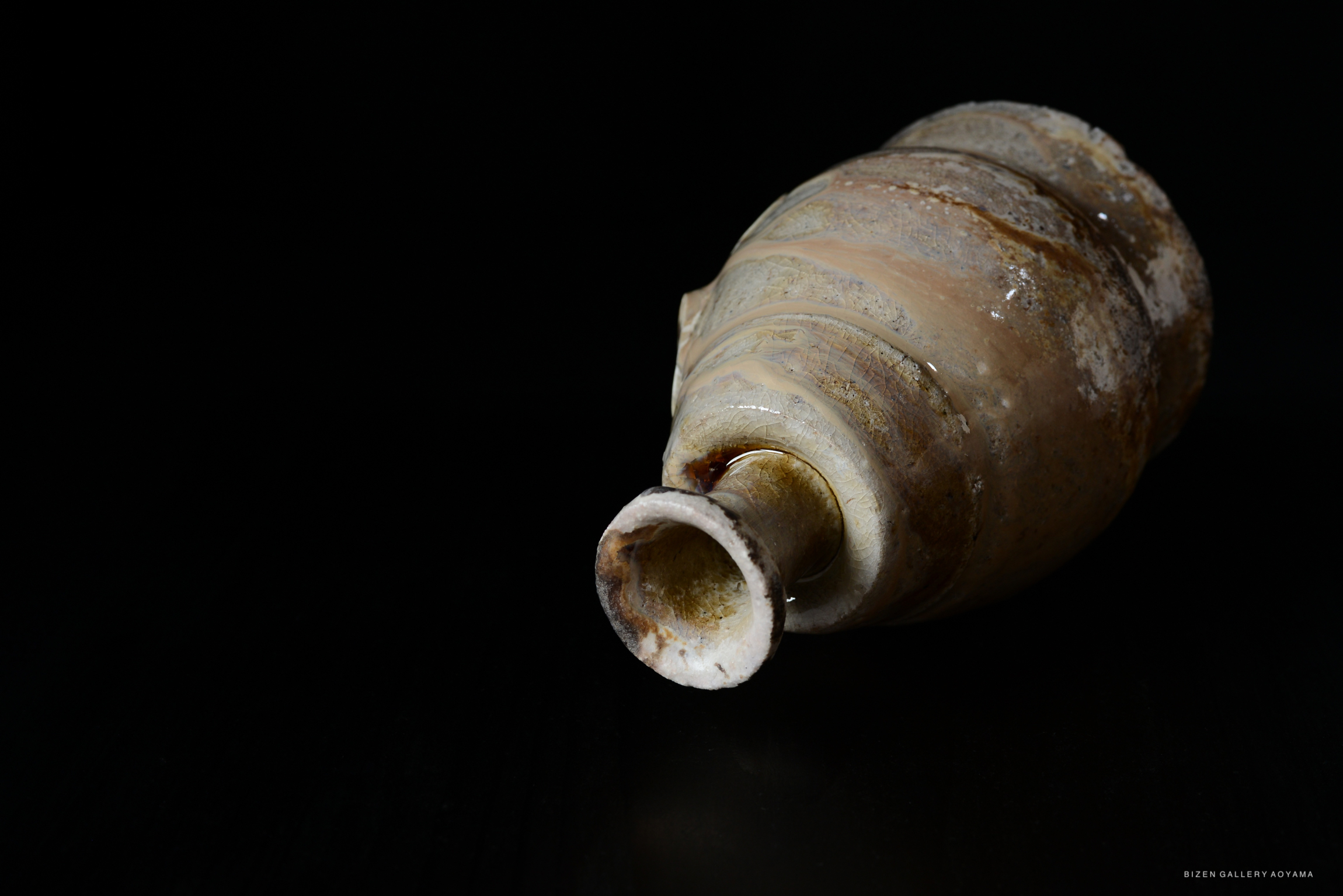 A traditional Japanese Shiro Tokkuri (white sake bottle) with a spiral design, resting on a black surface.