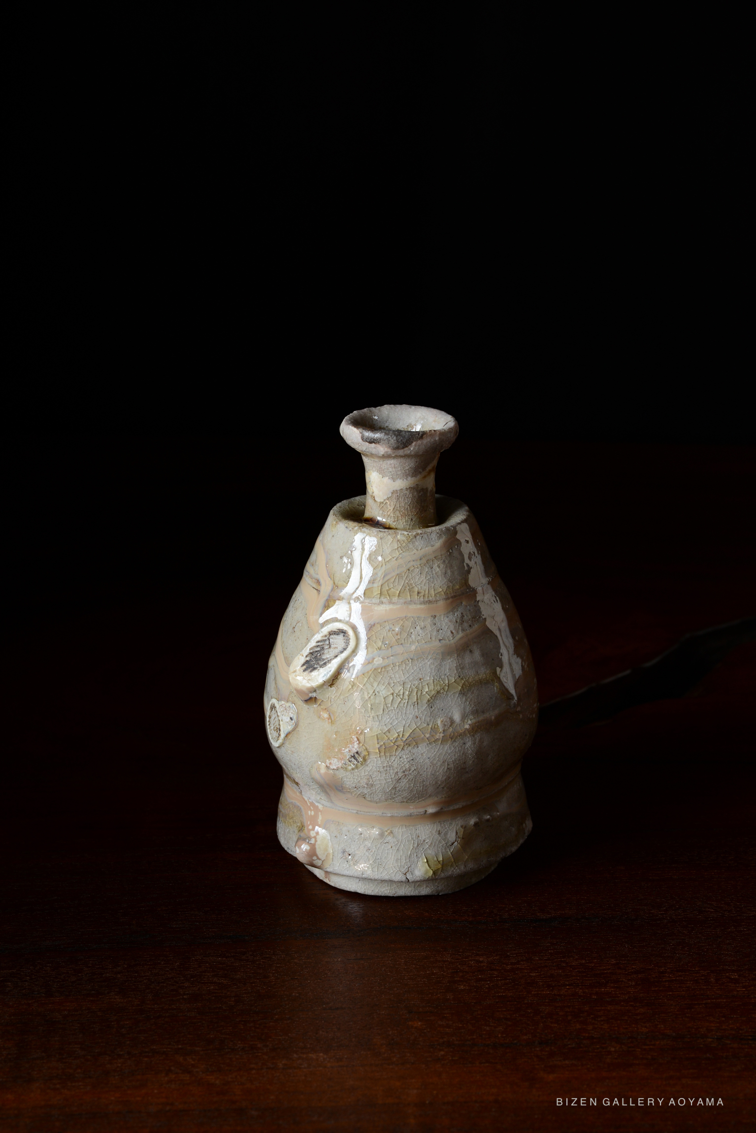 A ceramic Tokkuri with a unique shape and surface texture, displayed on a wooden table against a dark background.