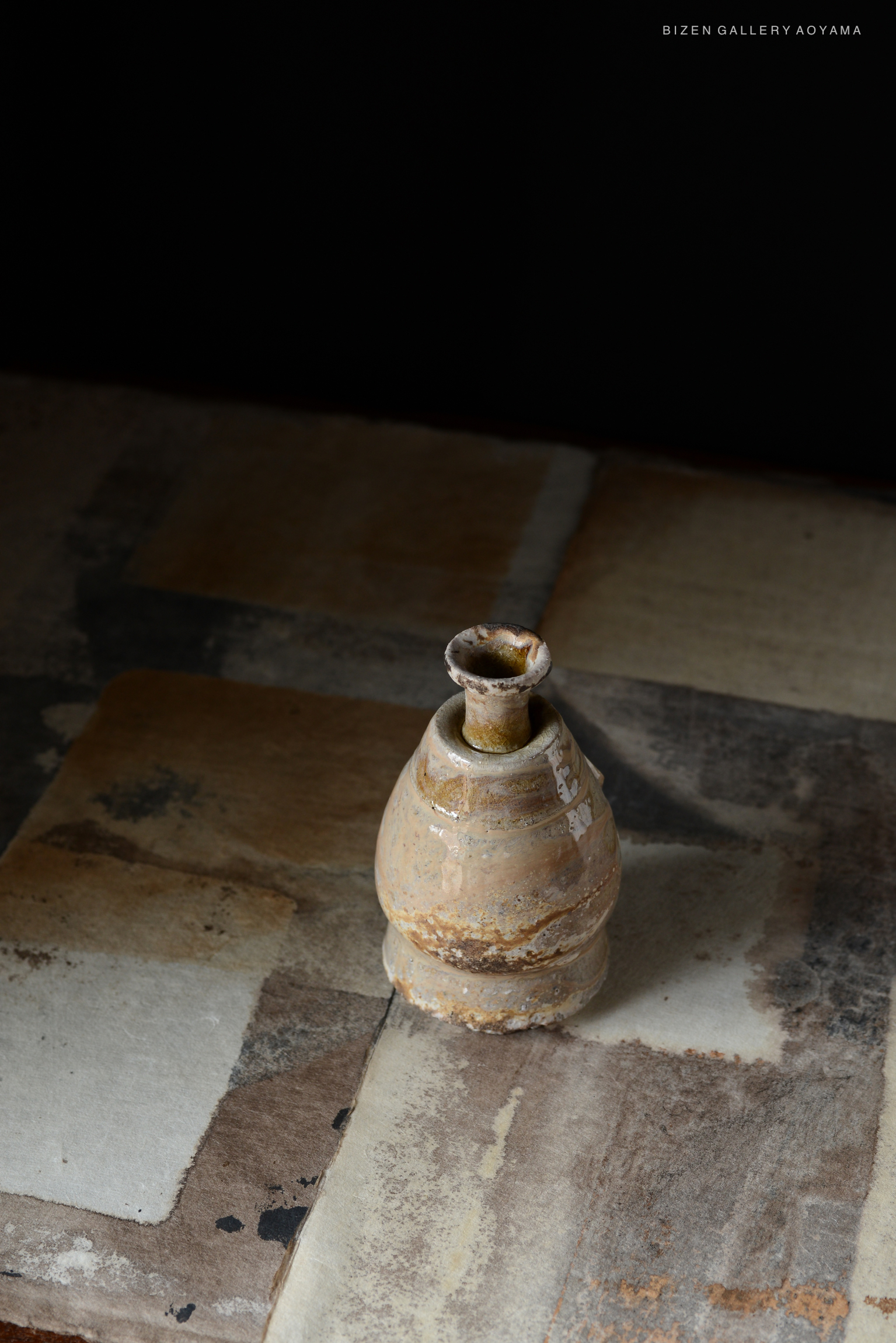 A Bizen pottery Shiro Tokkuri, or Japanese sake bottle, placed on a textured surface with a dark background.