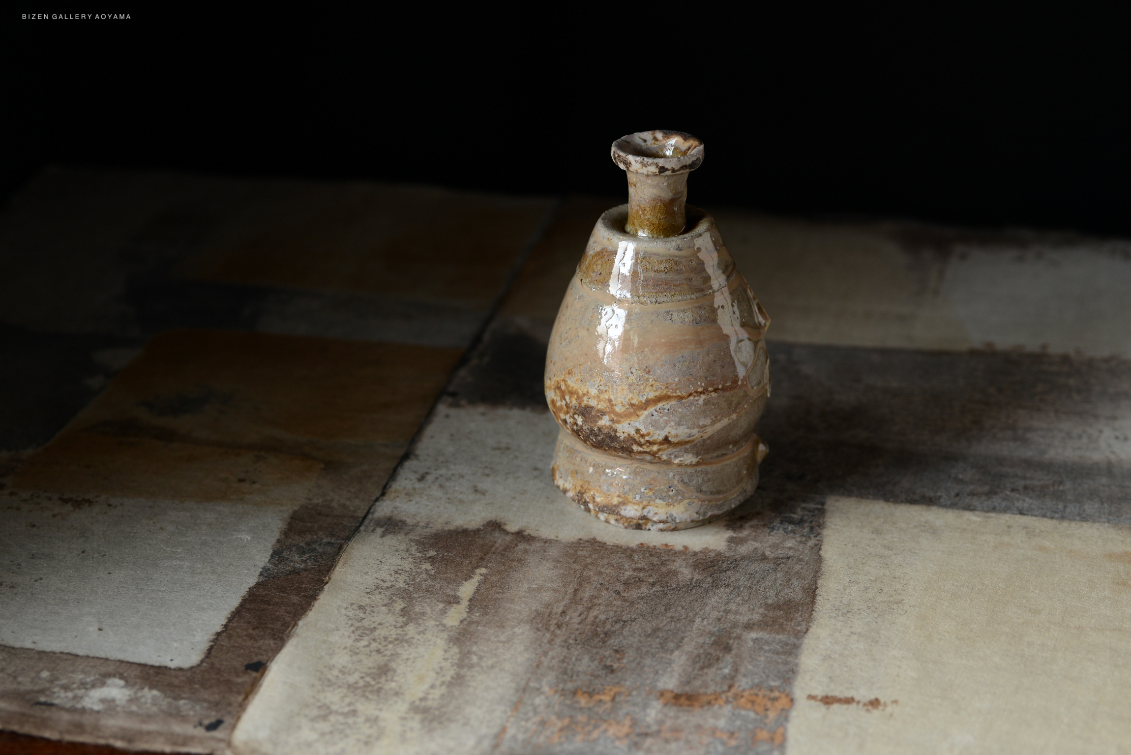A Shiro Tokkuri, a traditional Japanese sake vessel, displayed on a textured surface with earthy tones.