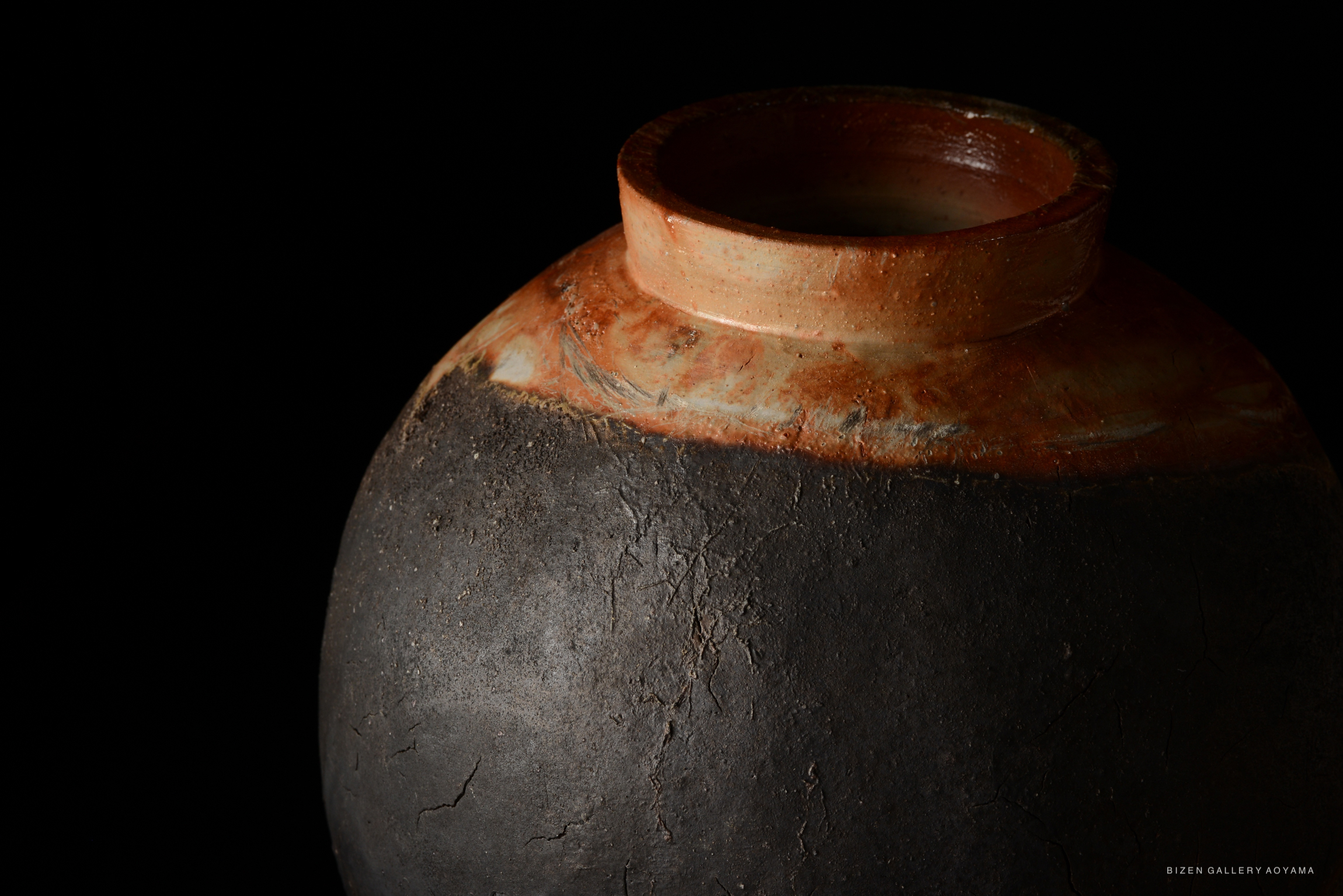 A close-up of a traditional Bizen pottery vase featuring a dark, textured surface and a smooth, light-colored rim.