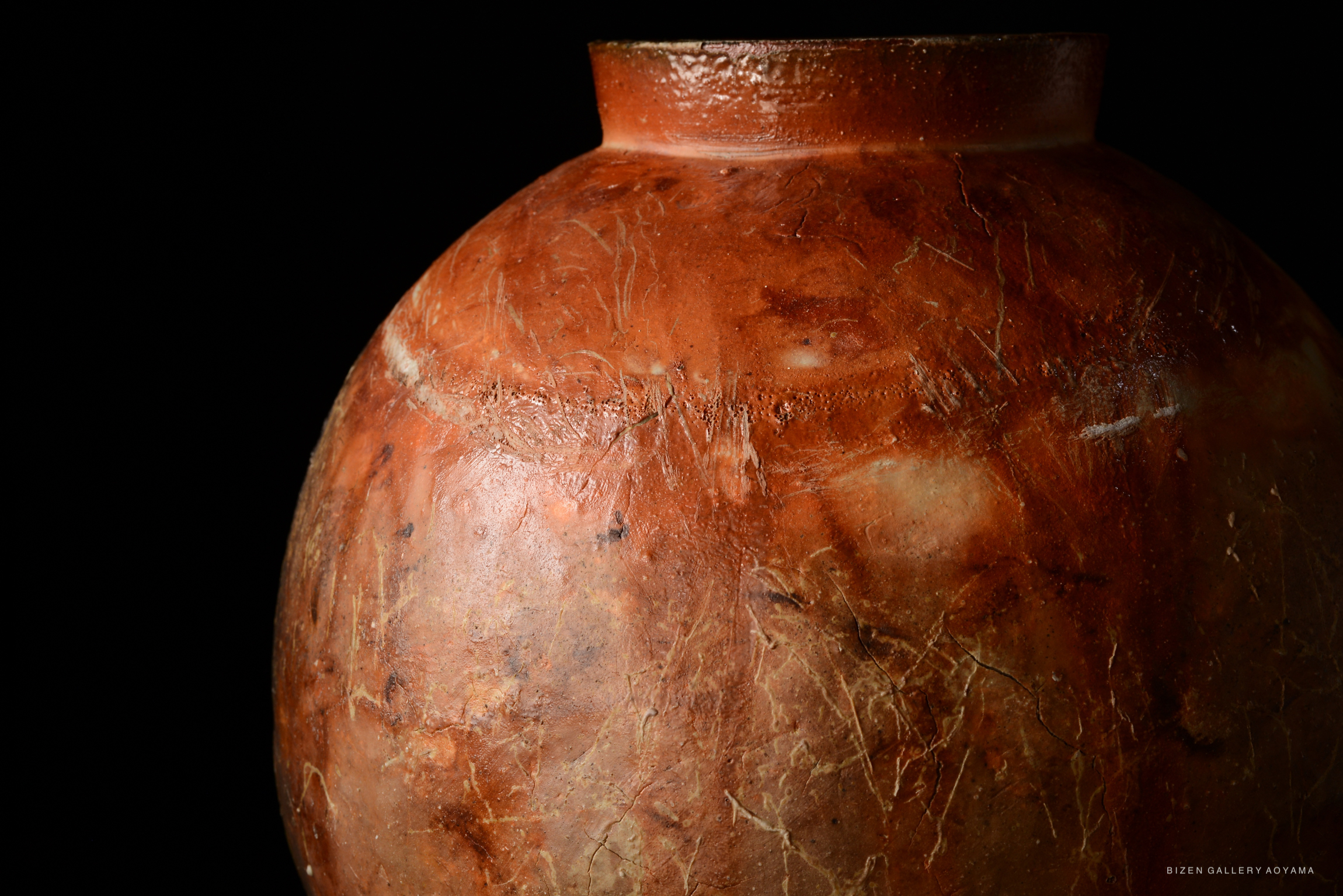 Close-up of a traditional Bizen pottery vase showcasing a textured, reddish-brown surface against a dark background.