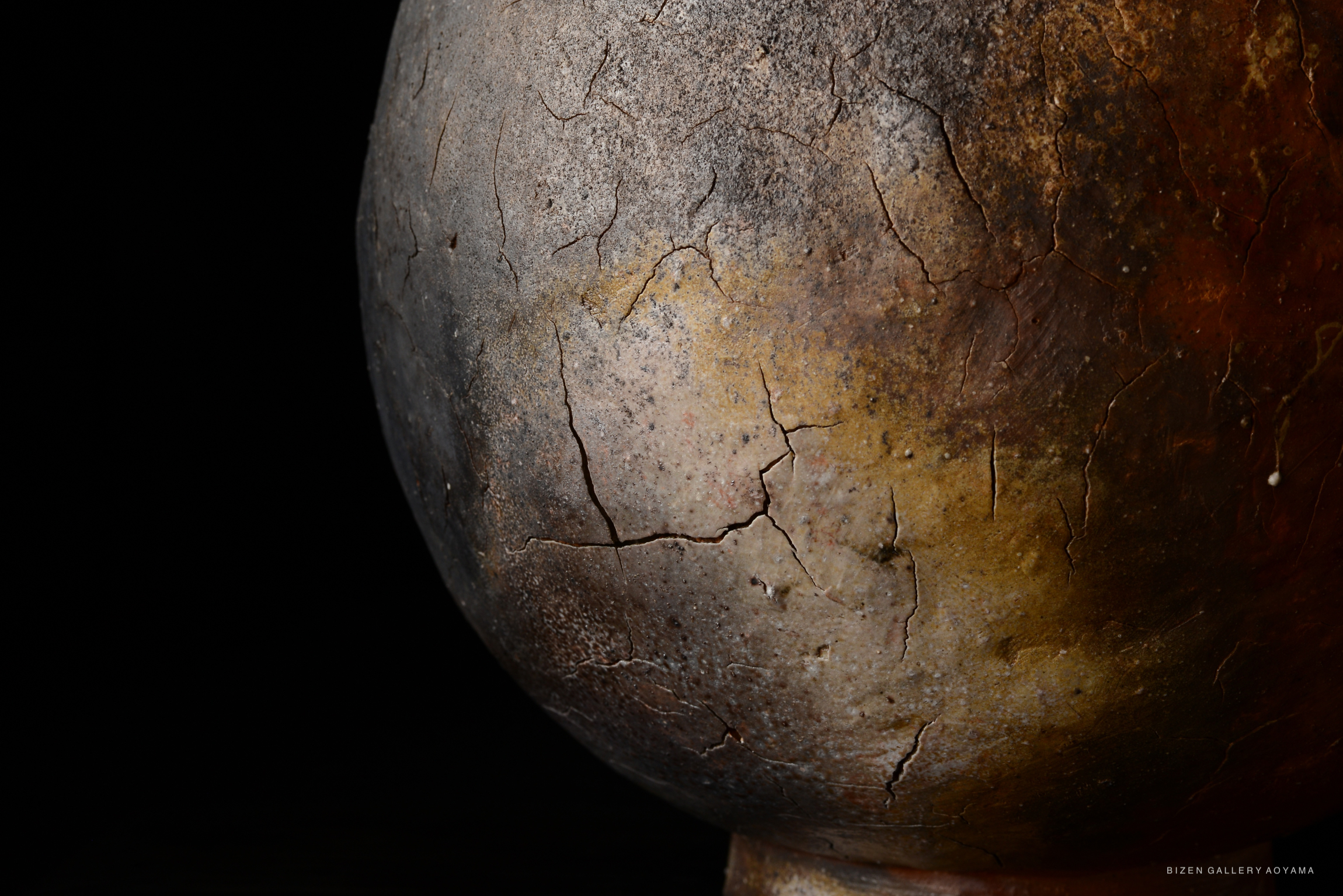 Close-up of a textured ceramic pot with cracks and earthy colors, set against a dark background.